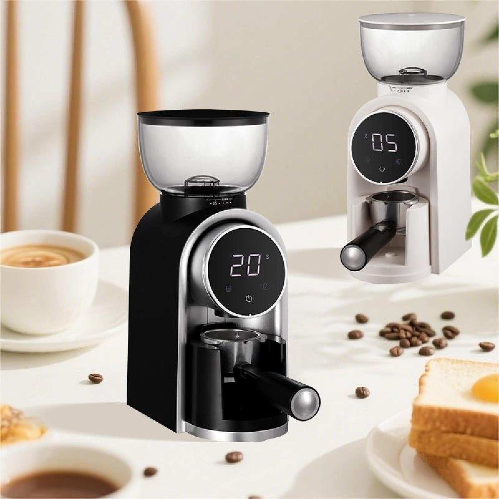 Zwei Kaffeemühlen, eine schwarz, eine weiß. Kaffeebohnen, Kaffeetasse und Toastscheiben liegen auf dem Tisch.