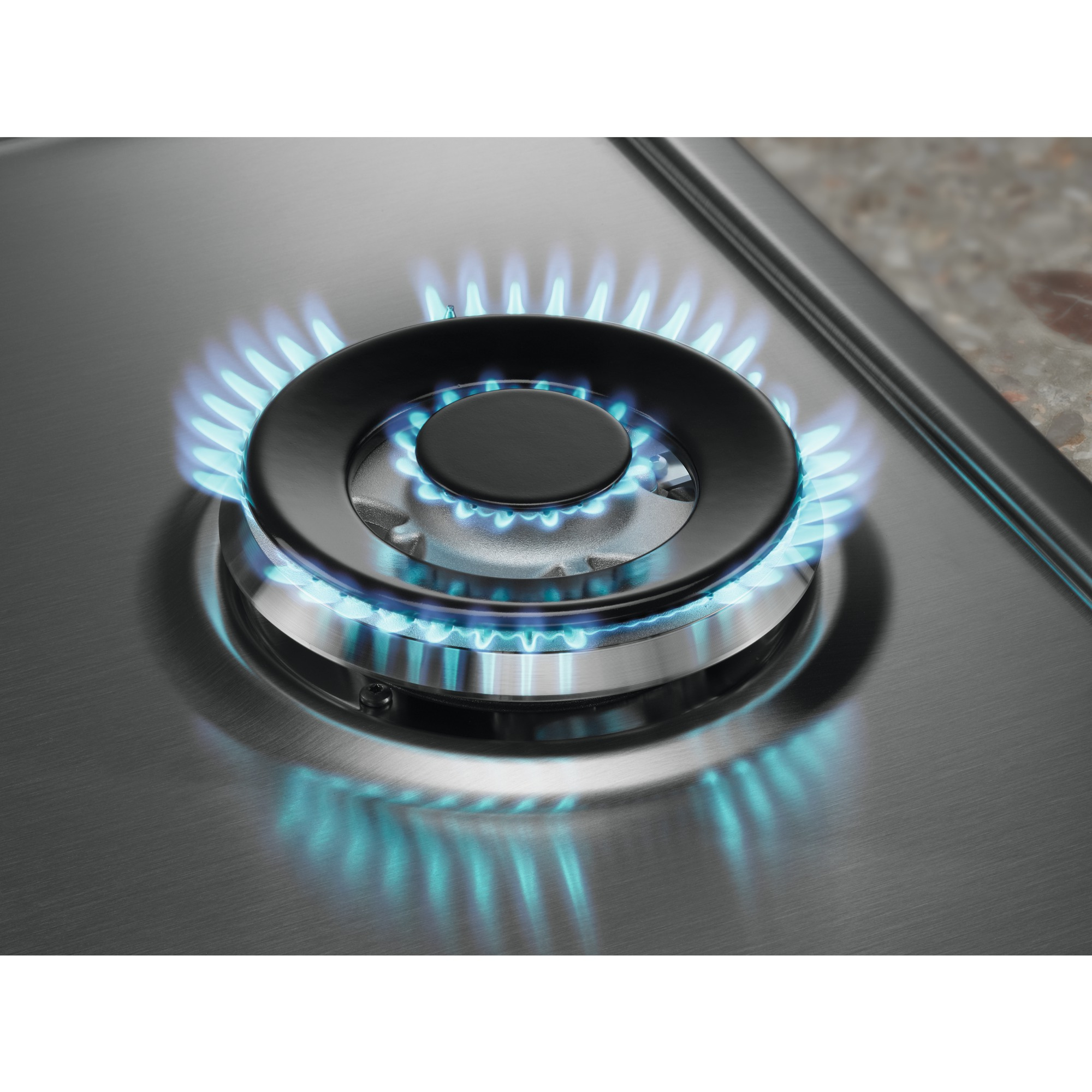 Primer plano de un quemador de estufa de gas con llamas azules, sobre una superficie de acero inoxidable. En el fondo, una encimera de piedra.