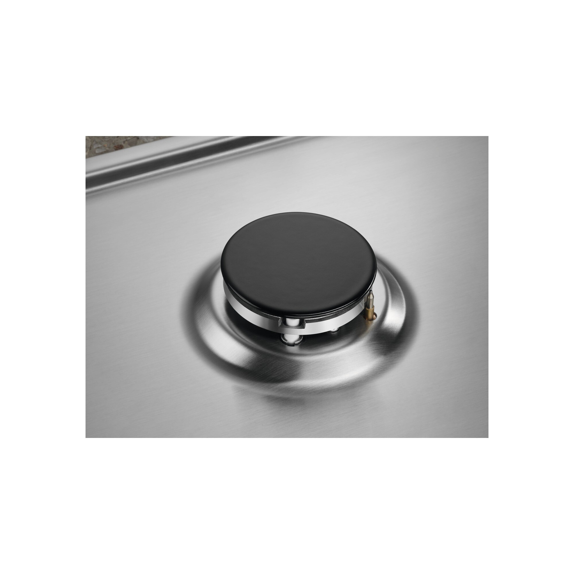 Zbliżenie palnika kuchenki gazowej. Czarny przycisk znajduje się na metalowej powierzchni. Mały kawałek metalu wystaje.