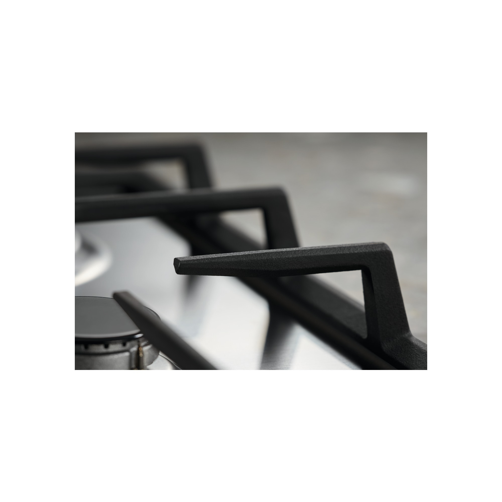 Zbliżenie czarnego rusztu kuchenki. Widoczna powierzchnia ze stali nierdzewnej i palnik. Rozmyte tło.