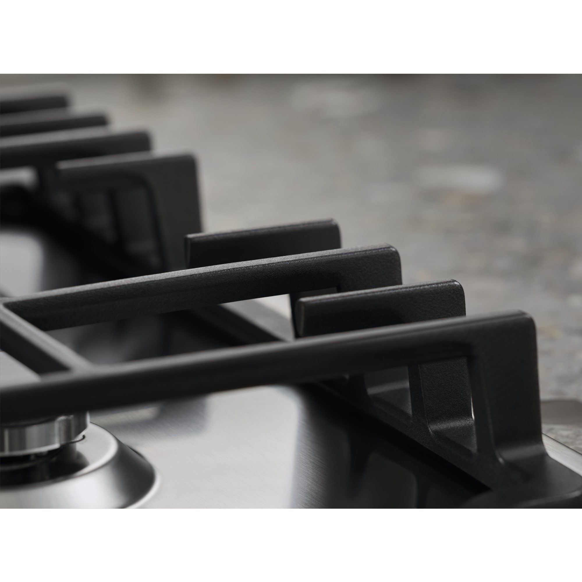 Zbliżenie czarnej kratki kuchenki na powierzchni ze stali nierdzewnej. Szary blat w tle.