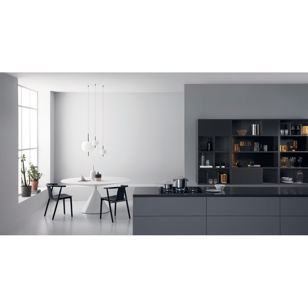 Cocina moderna con mesa blanca, sillas negras y armarios grises. Utensilios de cocina en la estufa. Plantas en una ventana. Estantes llenos.