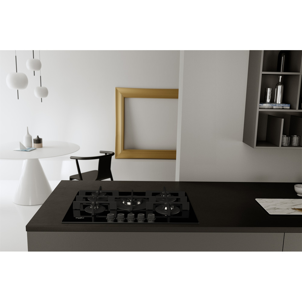 Cocina moderna con vitrocerámica negra, mesa blanca, silla negra, arte enmarcado en dorado y armarios grises. Diseño minimalista.