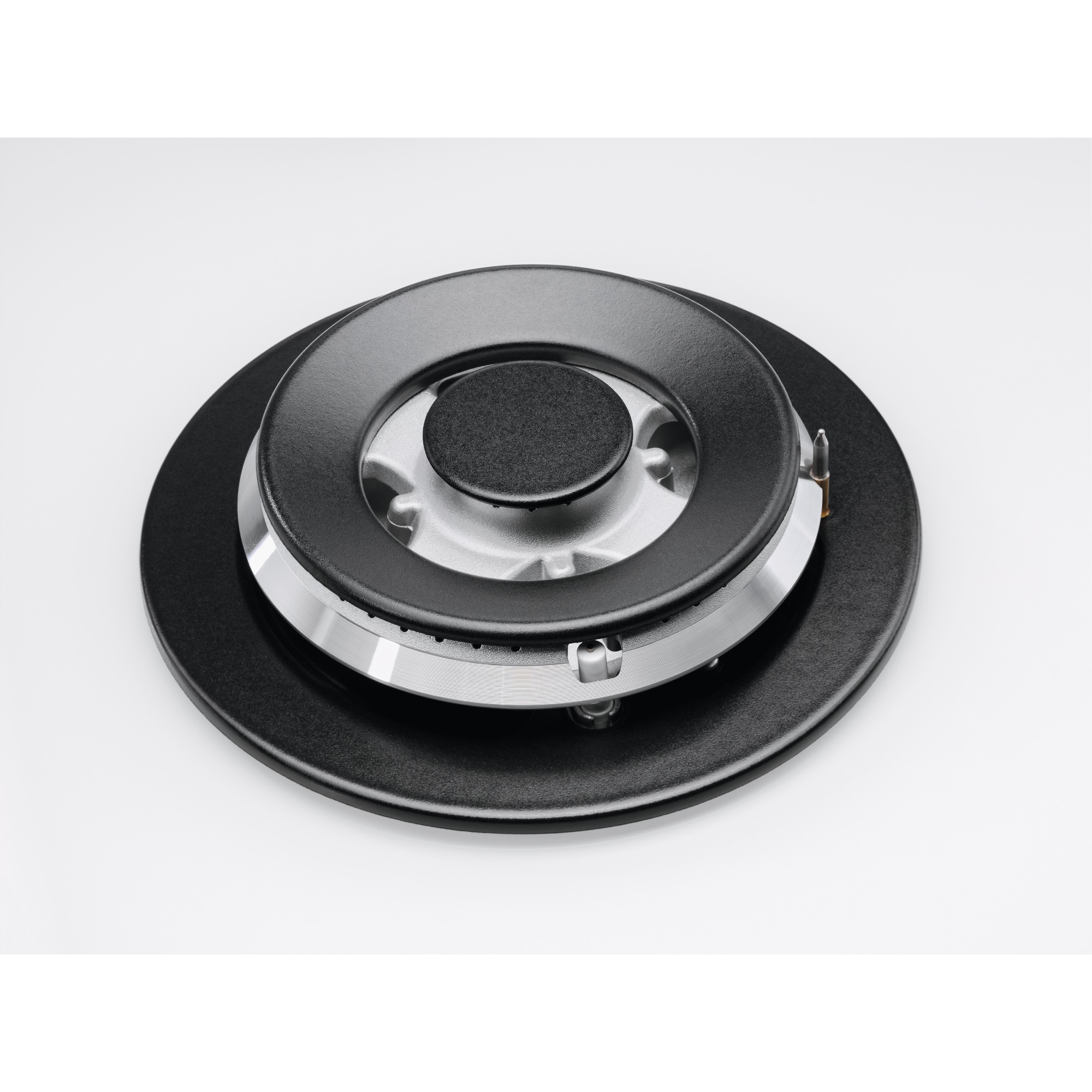 Zbliżenie czarnego palnika kuchenki gazowej. Ma okrągły kształt. Tło jest białe.