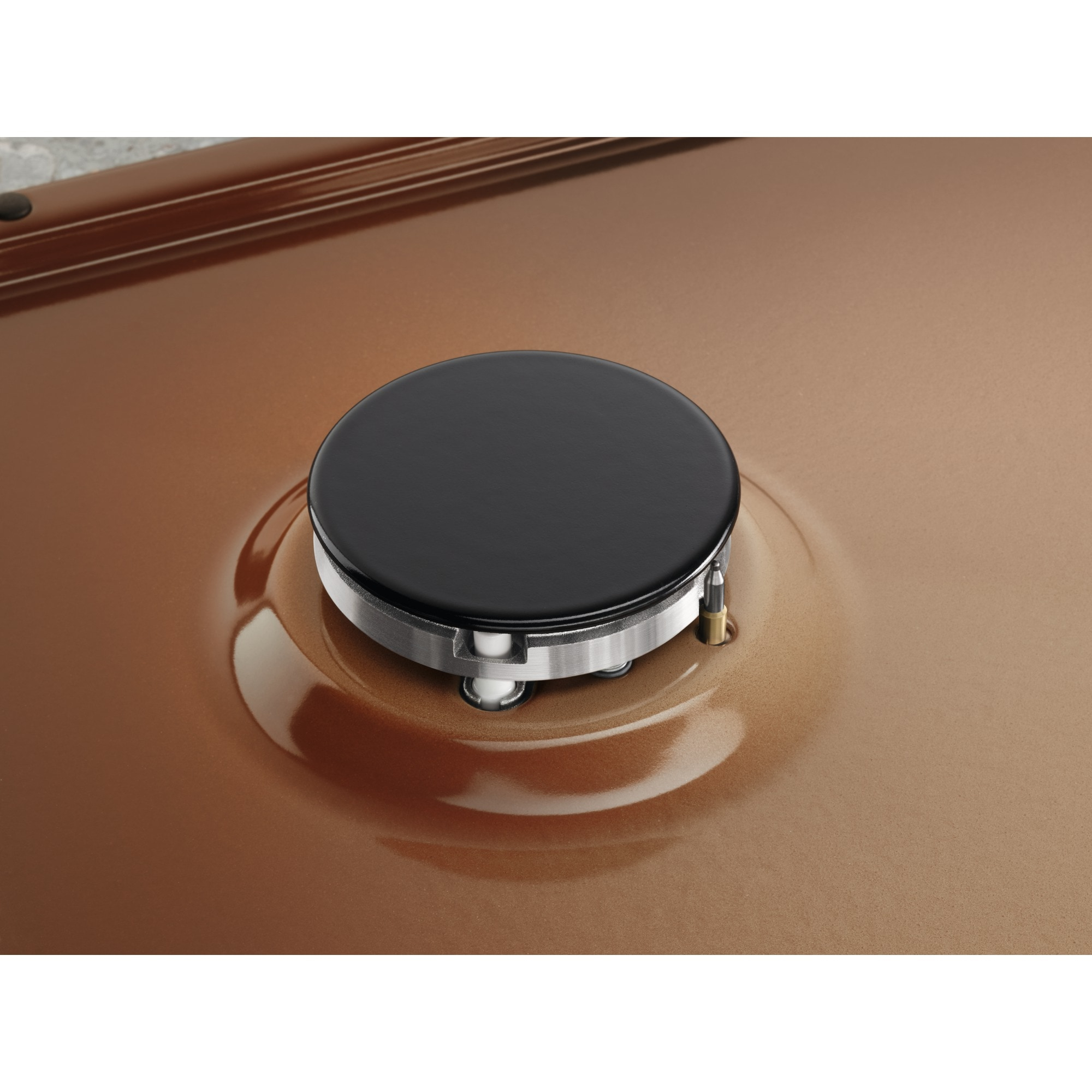 Primo piano di un fornello. Un bruciatore nero su una superficie marrone. Un anello di metallo circonda il bruciatore.