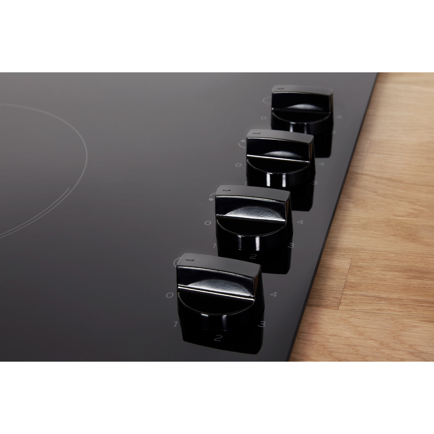 Una encimera eléctrica negra con cuatro perillas negras. La encimera está sobre una superficie de madera. Los números son visibles junto a las perillas.