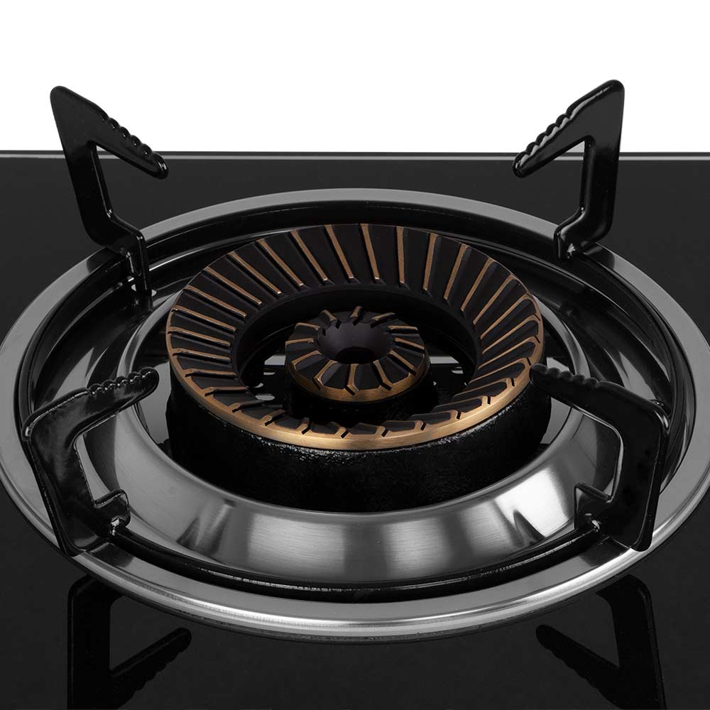 Primer plano de un quemador de cocina de gas. Quemador negro con detalles en bronce. Anillo de acero inoxidable y superficie de vidrio negro. Cuatro soportes negros.