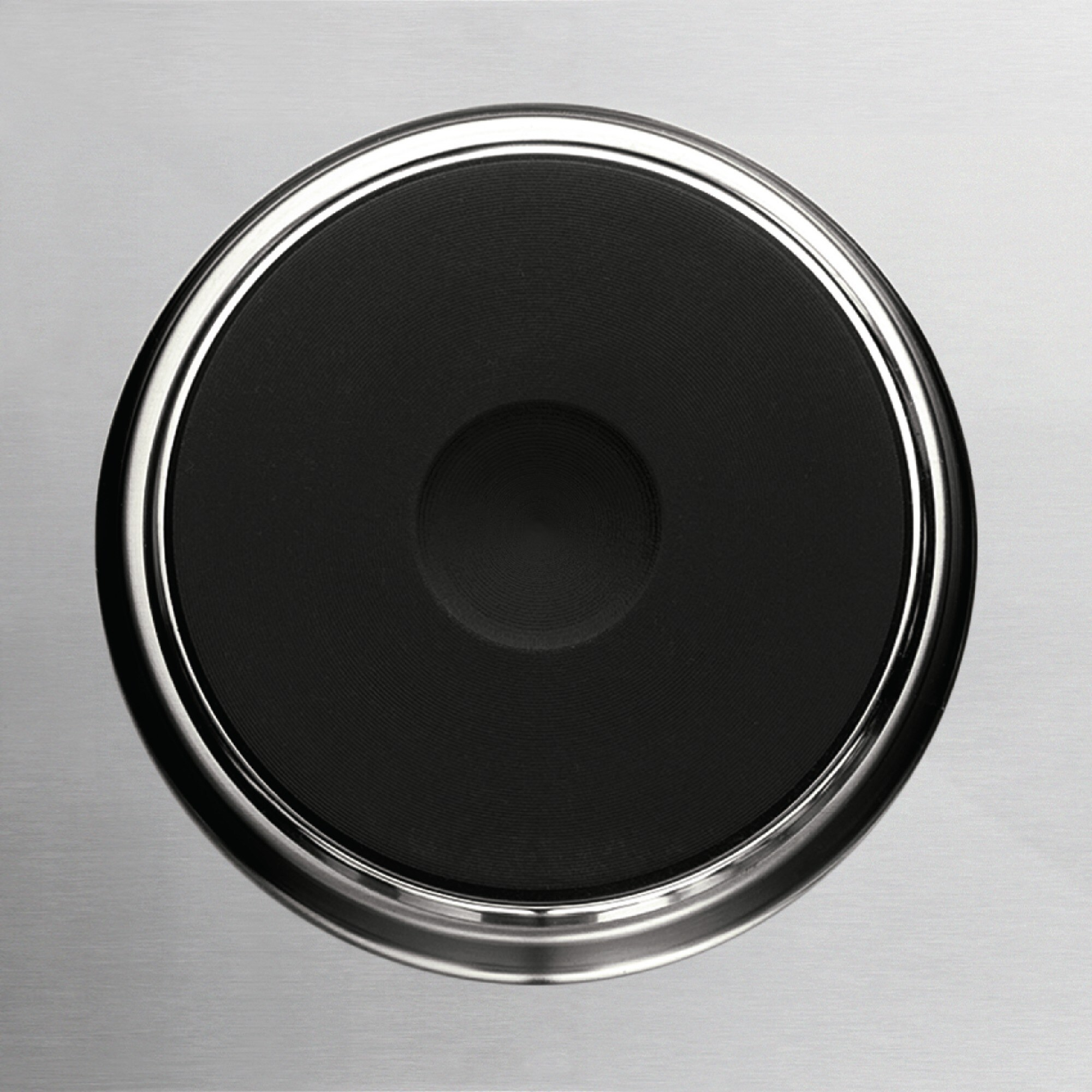 Zbliżenie czarnego palnika kuchenki elektrycznej ze srebrną obwódką, na srebrnej powierzchni. Palnik jest wyśrodkowany.