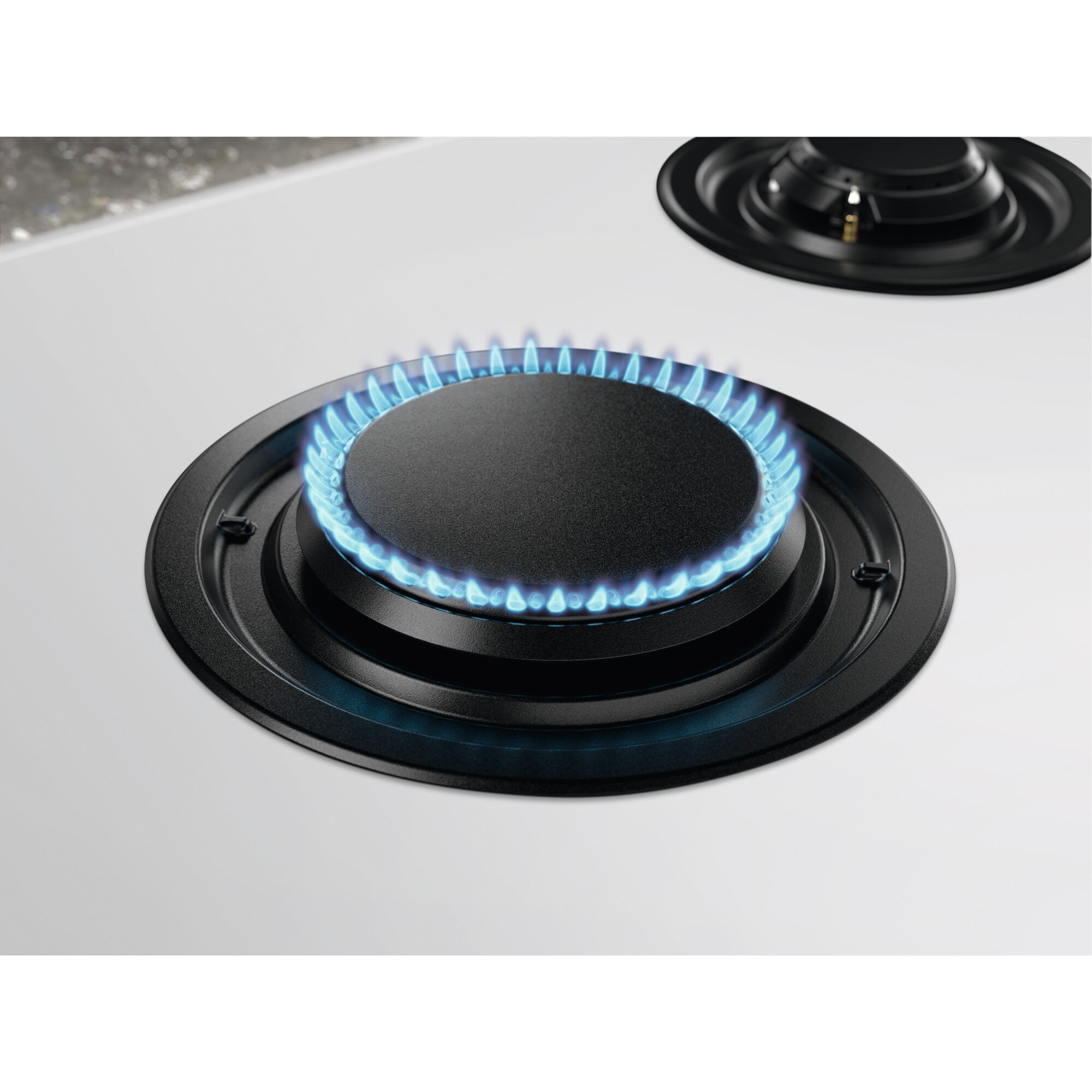 Primer plano de un quemador de estufa de gas con llamas azules. El quemador es negro, sobre una superficie blanca.