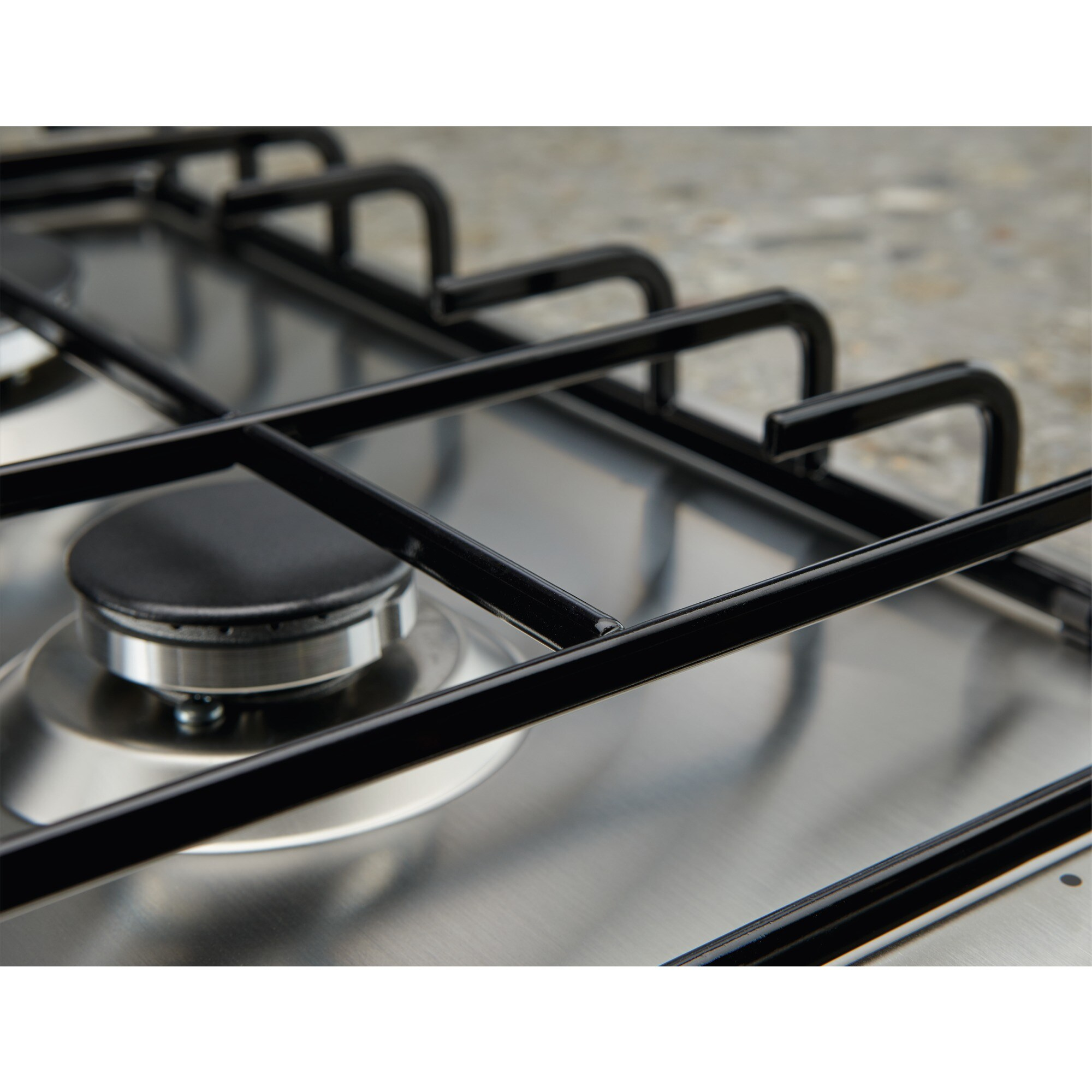 Zbliżenie kuchenki gazowej. Czarny metalowy ruszt nad srebrnym palnikiem. Tło rozmyte, jasnoszara nakrapiana powierzchnia.