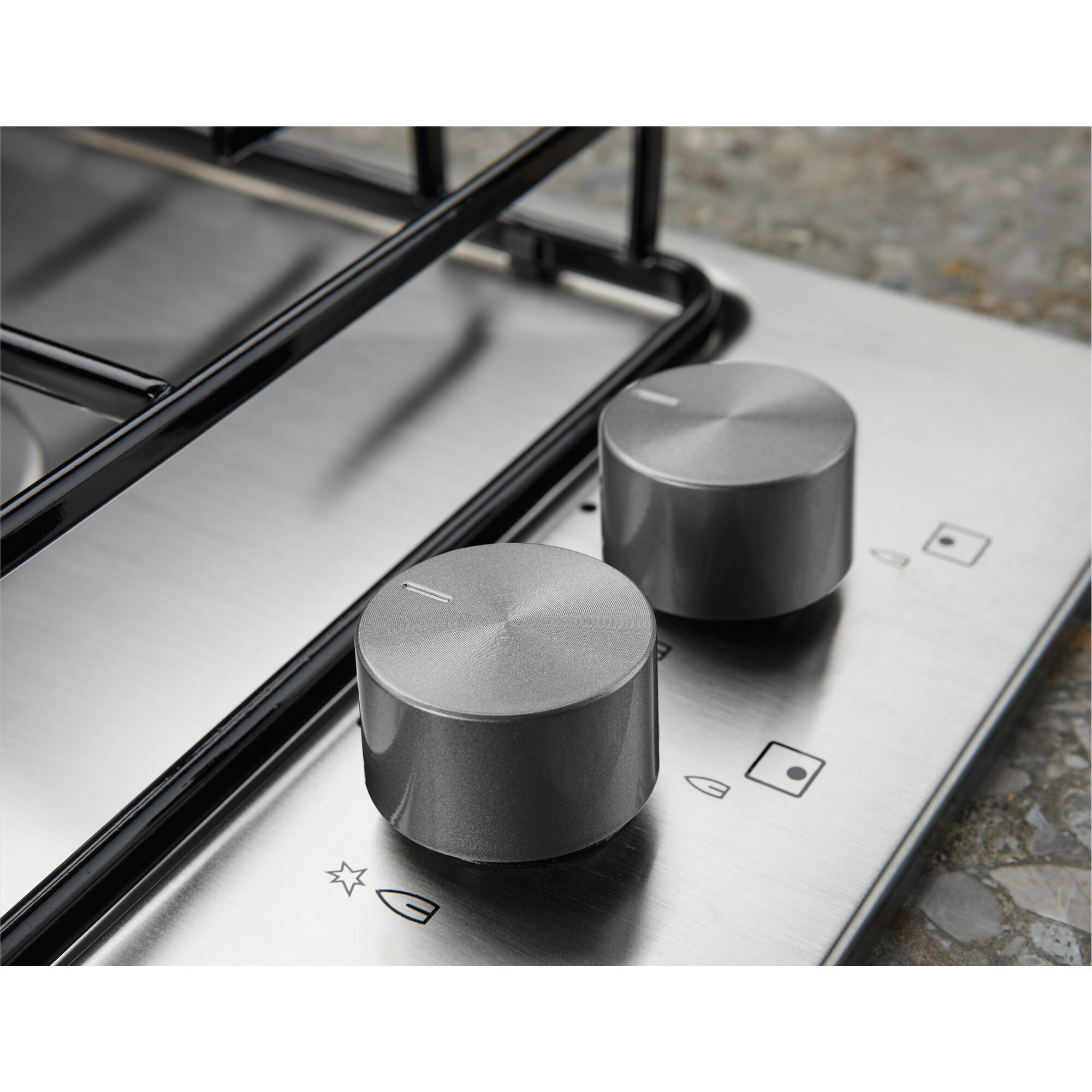 Zbliżenie na kuchenkę ze stali nierdzewnej z dwoma szarymi pokrętłami. Pokrętła mają wskaźnik linii.