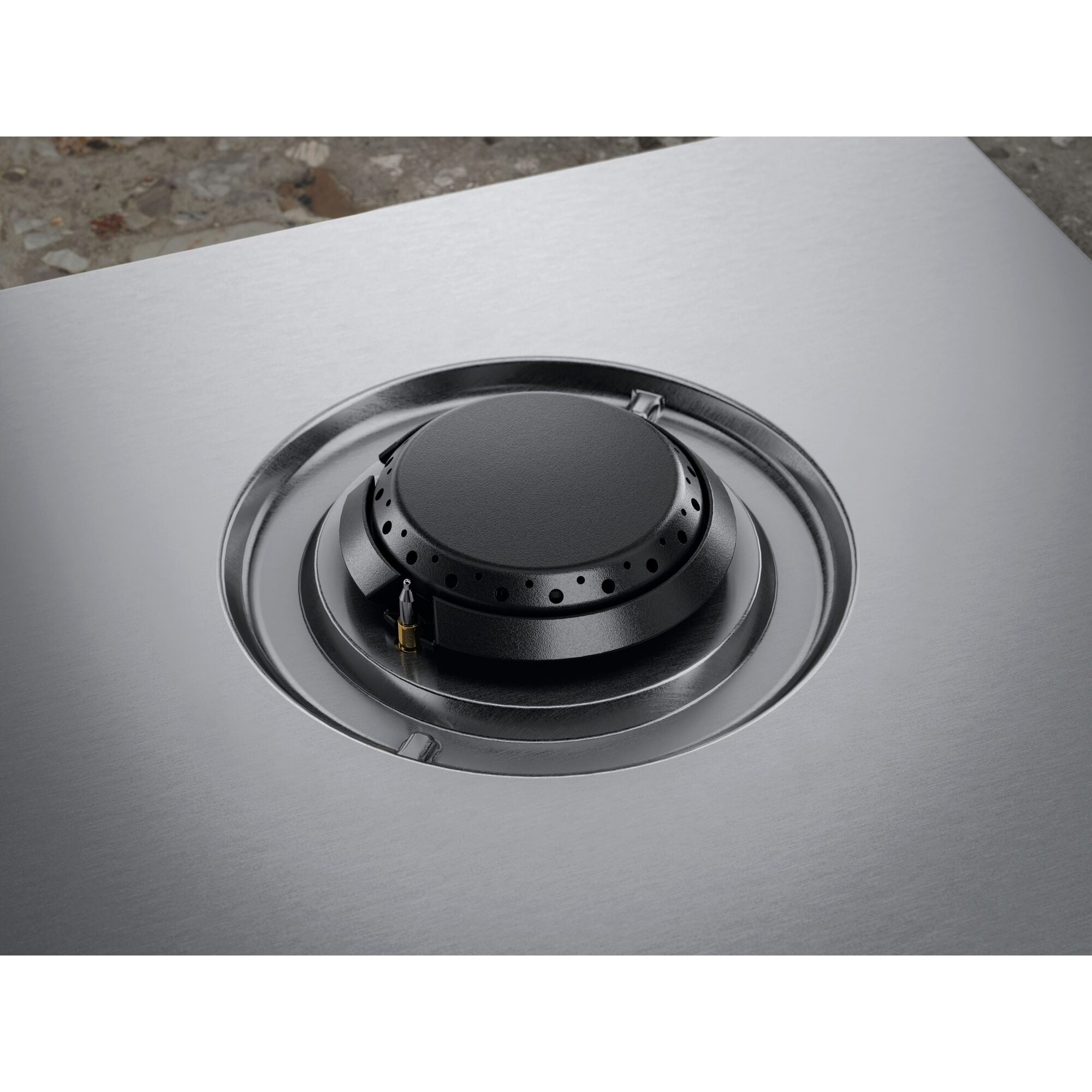 Zbliżenie czarnego palnika gazowego na powierzchni ze stali nierdzewnej. Palnik ma okrągły kształt z wieloma otworami.