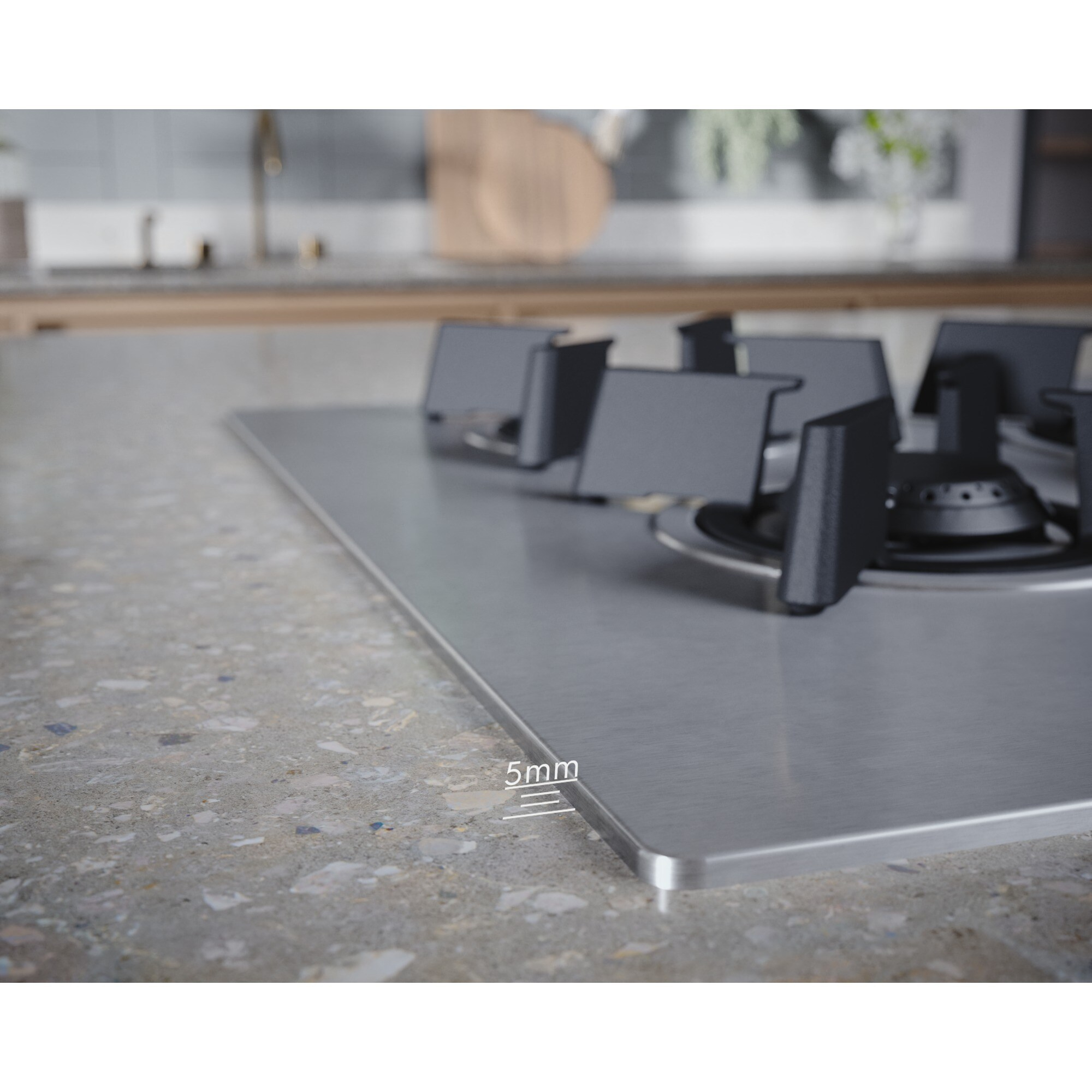 Zbliżenie płyty kuchennej ze stali nierdzewnej z czarnymi palnikami, na nakrapianym szarym blacie. Krawędź ma grubość 5 mm.