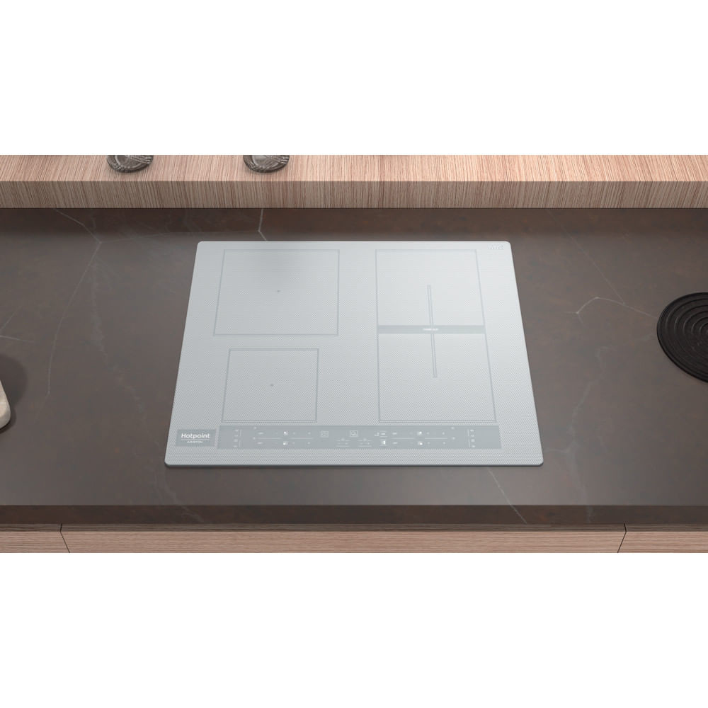 Un moderno piano cottura a induzione bianco Hotpoint è posizionato su un piano di lavoro scuro. Il piano cottura ha quattro fuochi e comandi touch. Lo sfondo include un ripiano in legno.