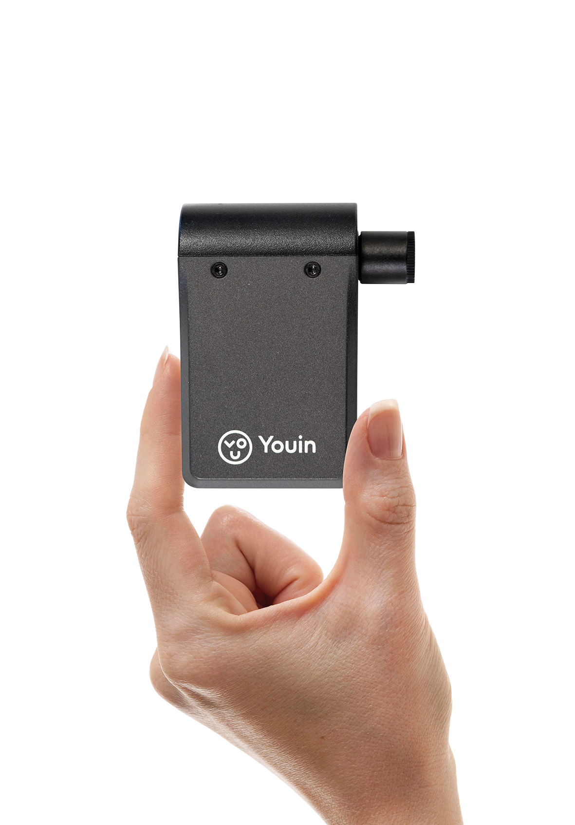 Una mano sostiene un pequeño dispositivo Youin gris oscuro. El dispositivo tiene un cuerpo rectangular con una extensión cilíndrica. Fondo blanco.
