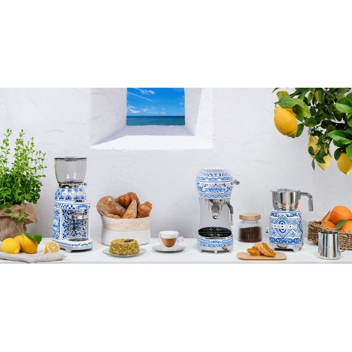 Una escena de cocina con máquinas de café, pan, pastel y limones. Paredes blancas, una ventana con vista al mar y un limonero completan la escena.