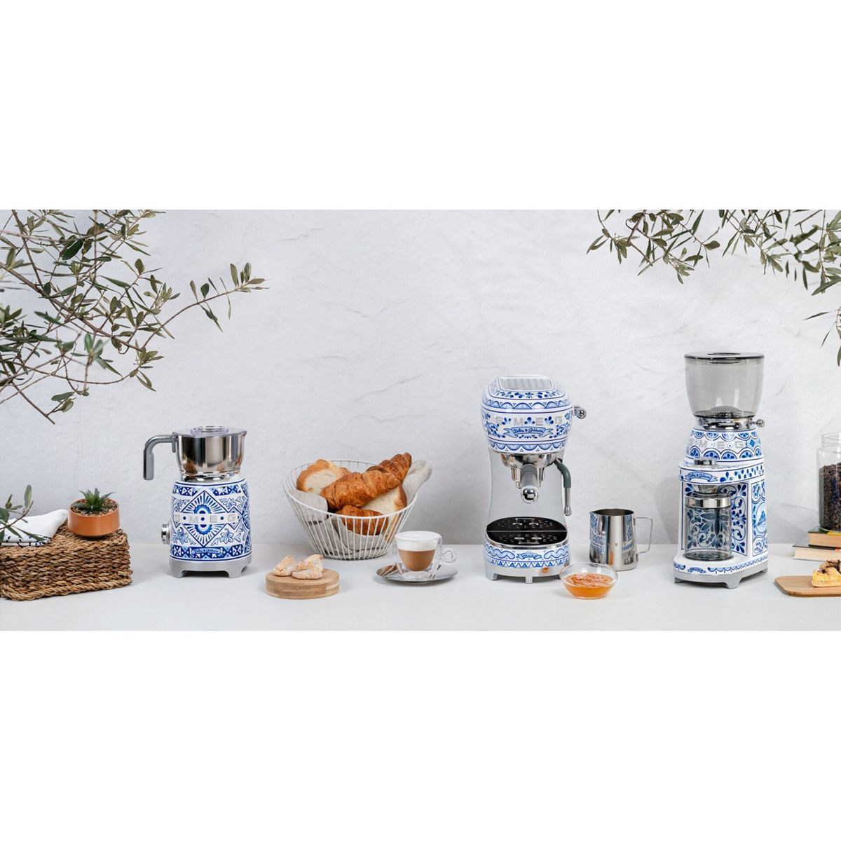 Una exhibición de máquinas de café, pan y tazas de espresso con un diseño floral blanco y azul. Se ve un tarro de granos de café.