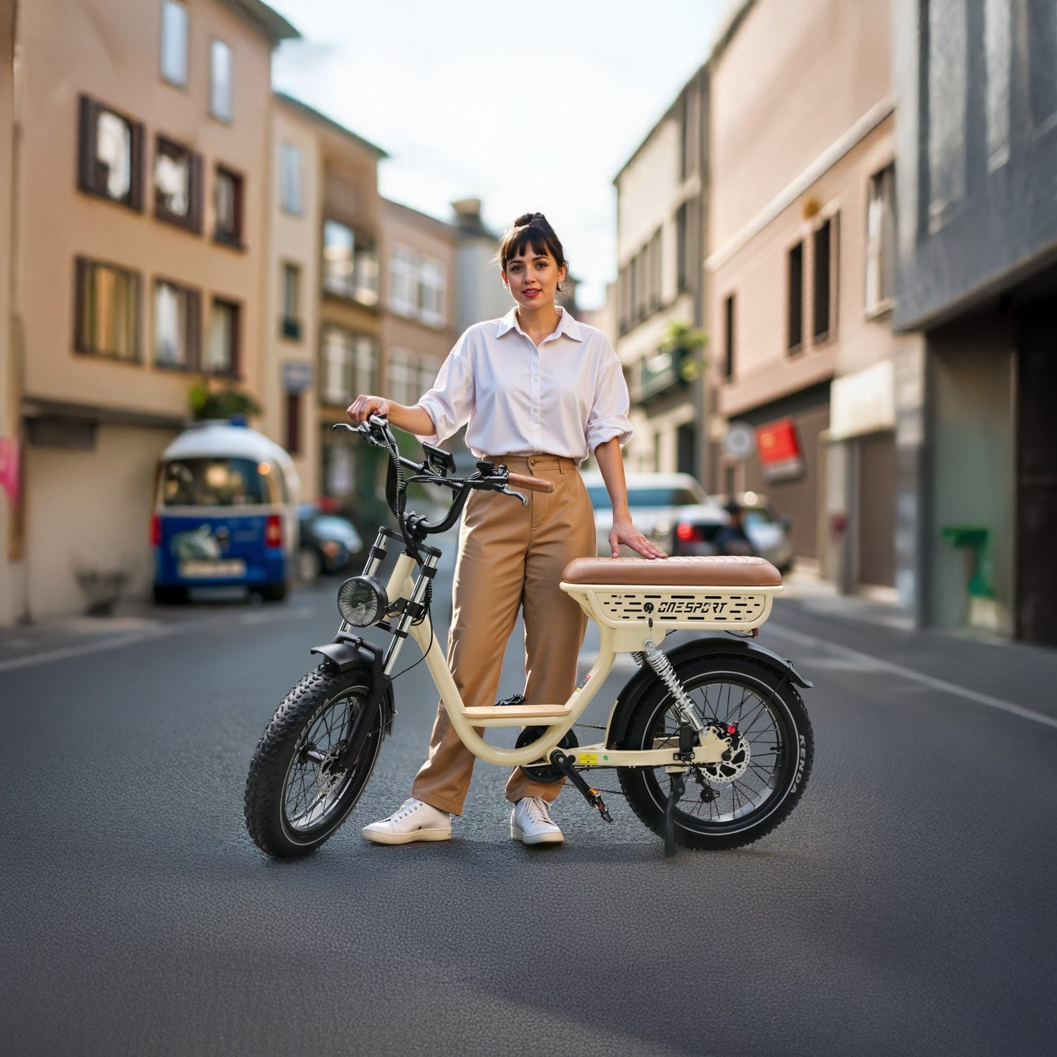 Eine Frau steht mit einem Elektrofahrrad auf einer Straße. Gebäude säumen die Straße. Das Fahrrad ist cremefarben und schwarz.