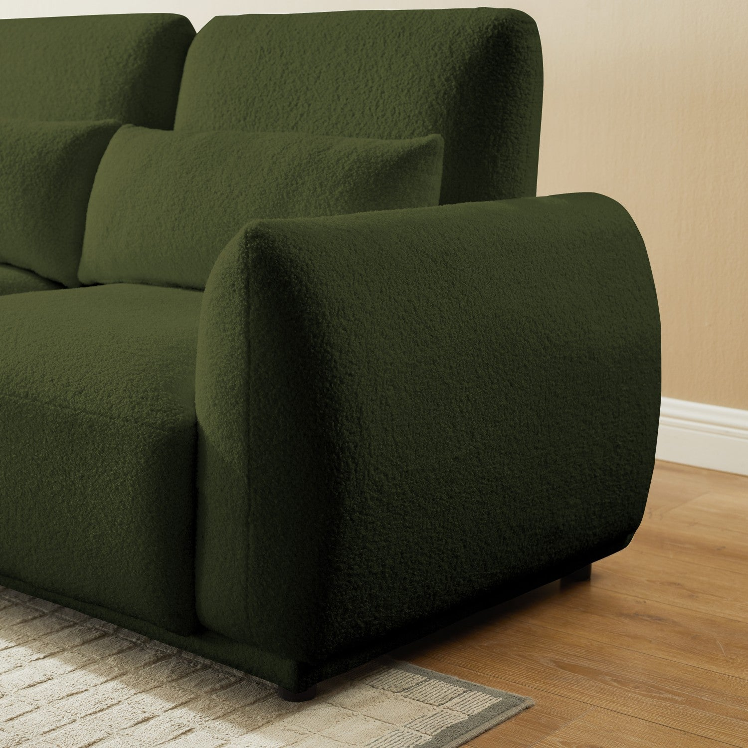 Un sofá verde oliva con dos cojines traseros y un reposabrazos. Está sobre un suelo de madera, con una alfombra abajo.