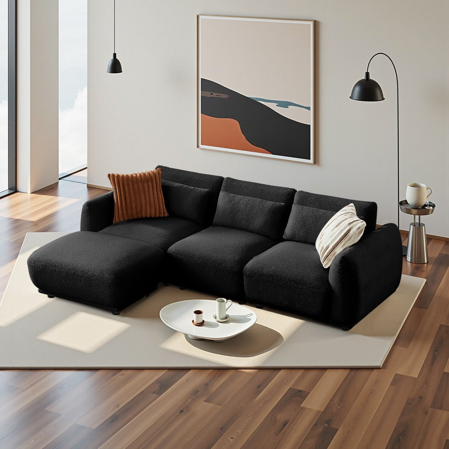 Ein modernes Wohnzimmer mit schwarzem Sofa, Kunstwerk und Lampe. Ein Couchtisch mit Tassen davor. Ein Teppich liegt auf dem Boden.