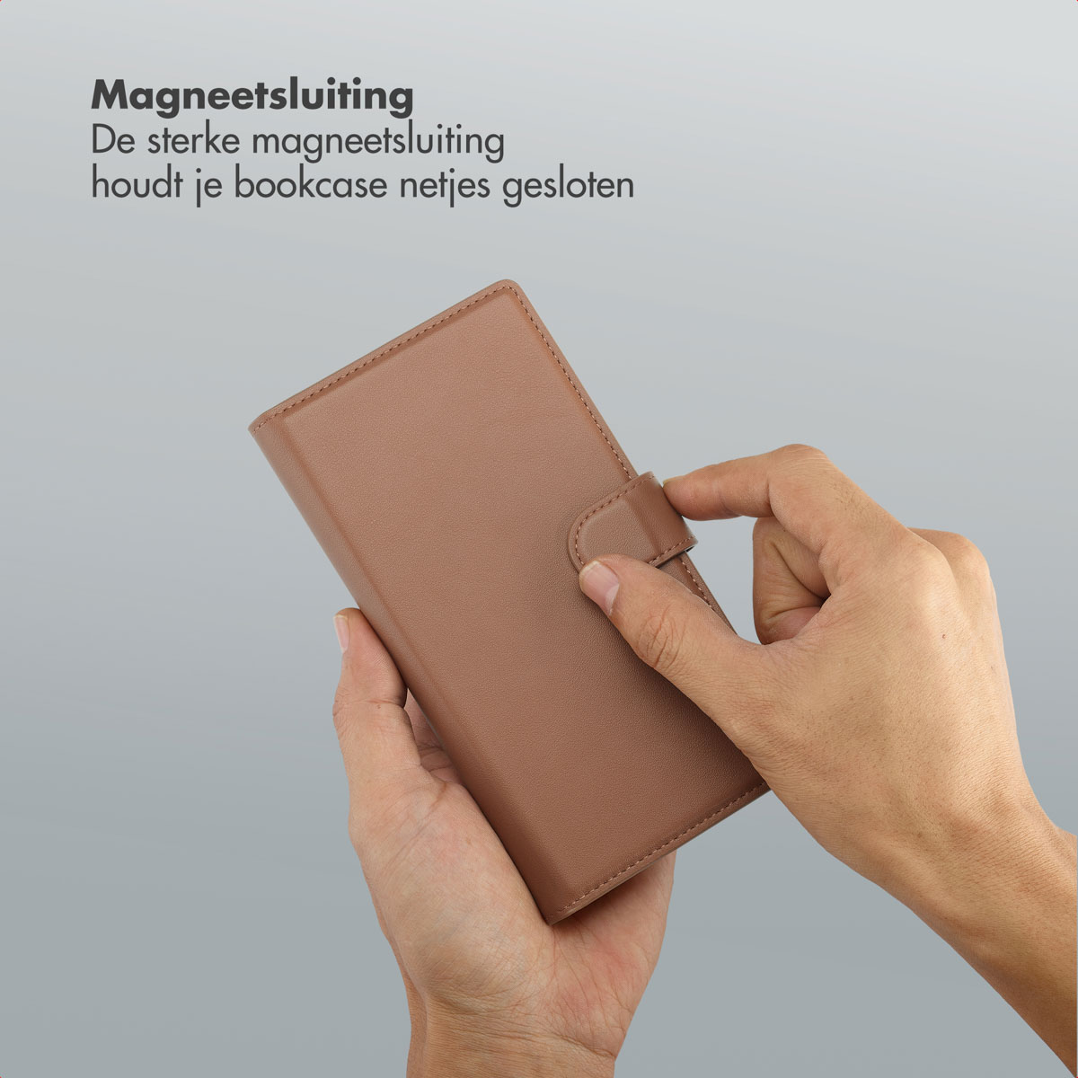 Handen houden een bruine leren hoes vast en sluiten de magnetische sluiting. De achtergrond is lichtgrijs.