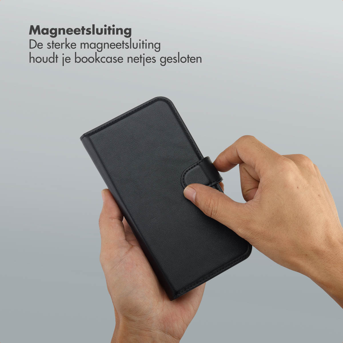 Een hand houdt een zwarte telefoonhoes met magneetsluiting vast. De hoes wordt door de hand gesloten op een grijze achtergrond.