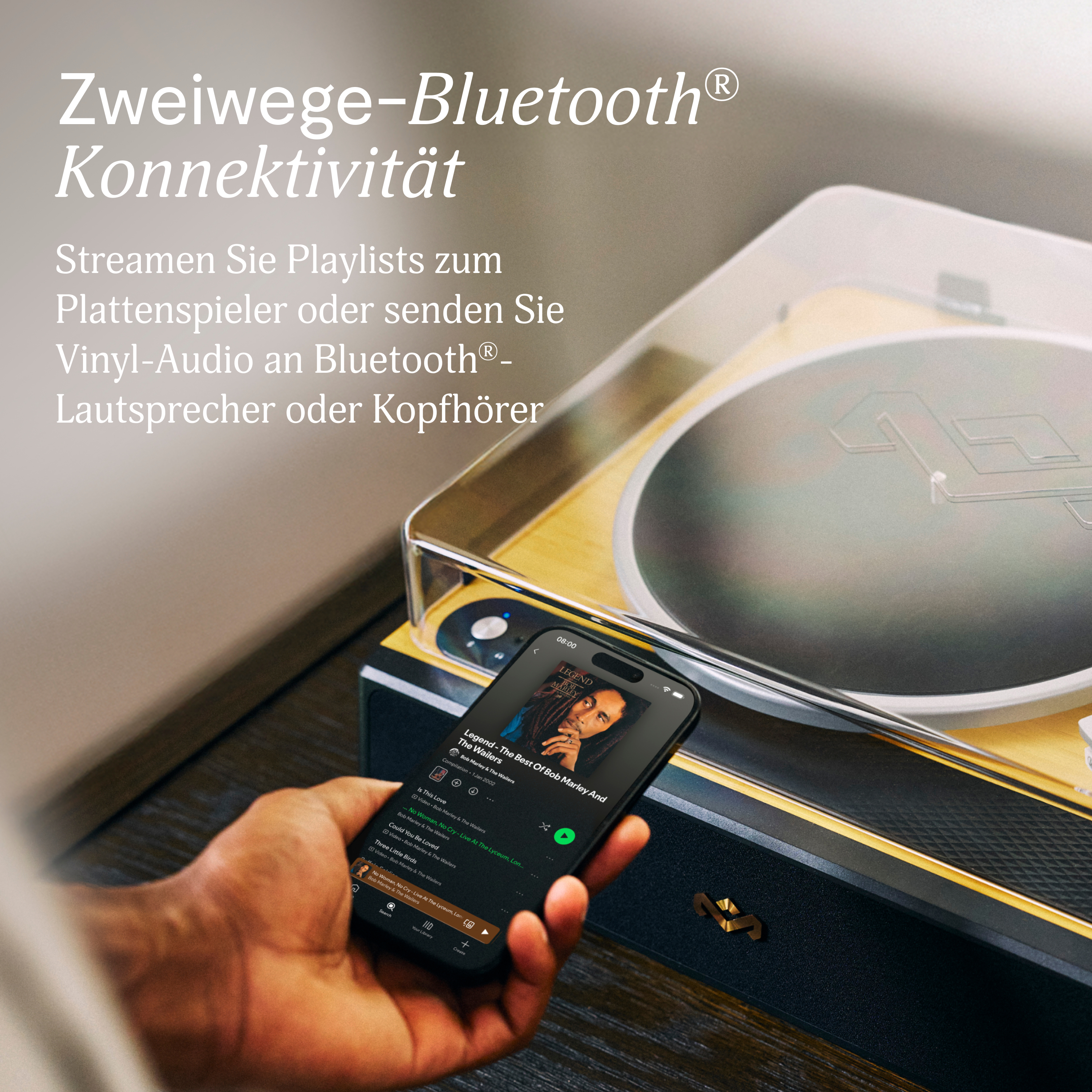 Plattenspieler mit Smartphone, das Bob Marley-Albumcover anzeigt. Hand hält das Telefon. Schwarz- und Goldtöne.