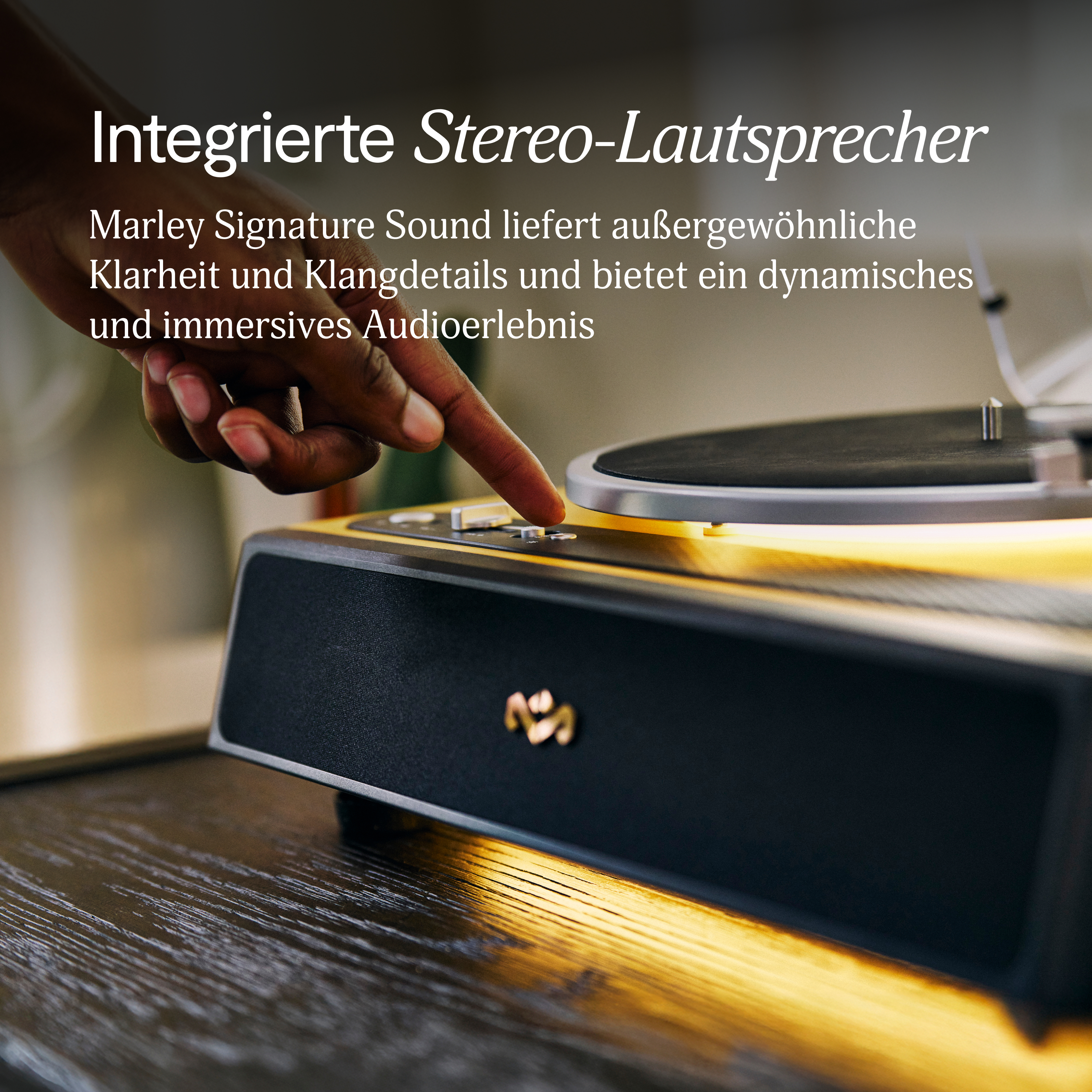 Eine Hand drückt eine Taste auf einem Plattenspieler. Ein Lautsprecher und ein Holztisch sind zu sehen. Text: 'Stereo-Lautsprecher'.