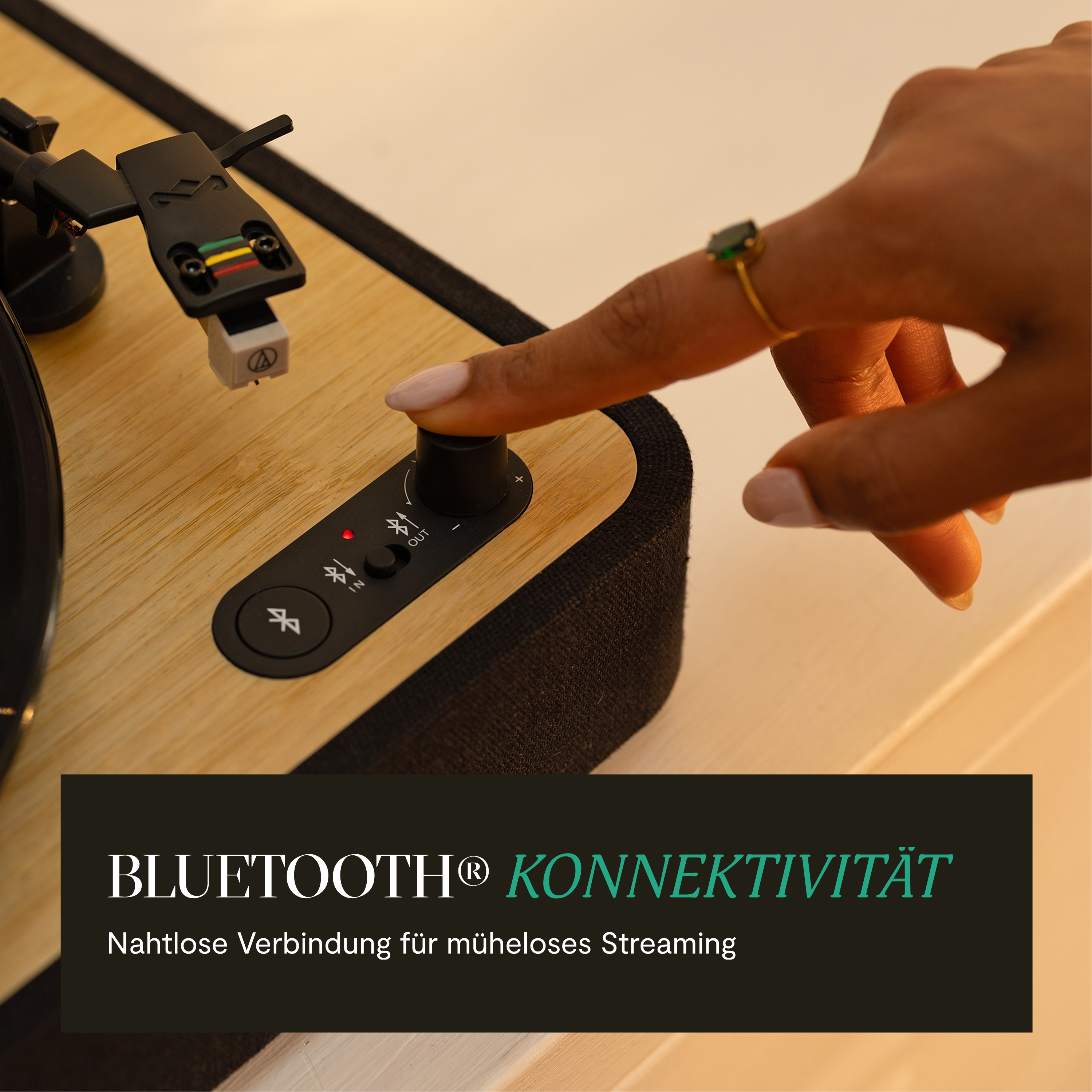 Eine Hand drückt auf eine Taste eines hölzernen Plattenspielers. Der Text lautet 'Bluetooth Konnektivität'.