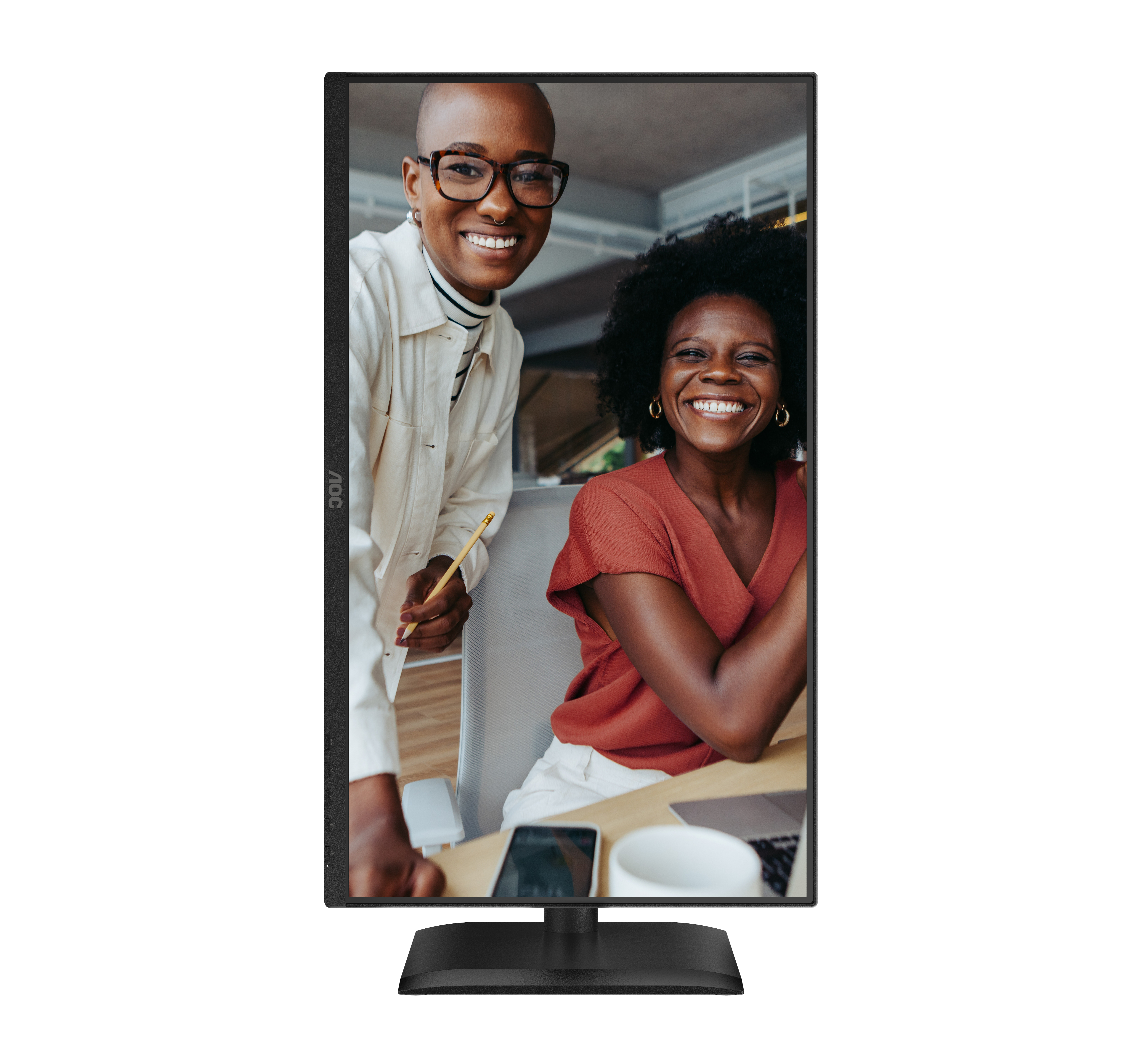 Twee lachende vrouwen voor een monitor. Eén houdt een potlood vast. Bureau met telefoon, laptop en beker.
