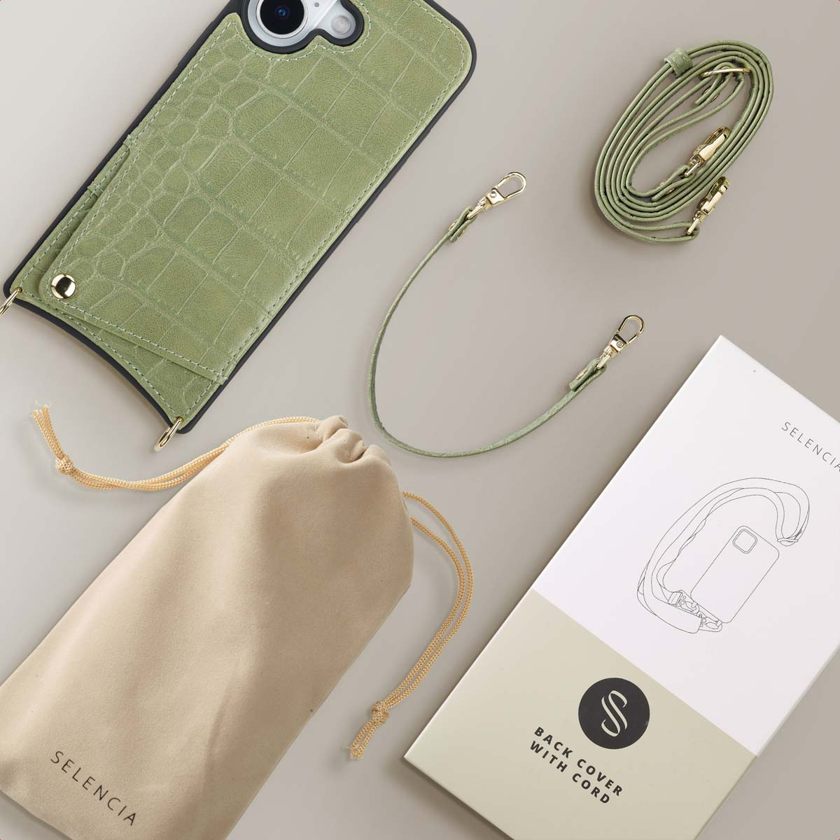 Een bovenaanzicht toont een groene telefoonhoes, riem, tas en doos. Op de doos staat: Back Cover With Cord en Selencia.