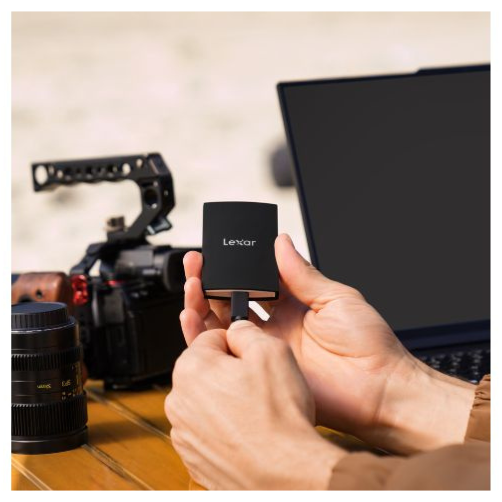 Osoba trzyma czarny dysk Lexar i podłącza go do laptopa. W tle aparat i obiektyw.