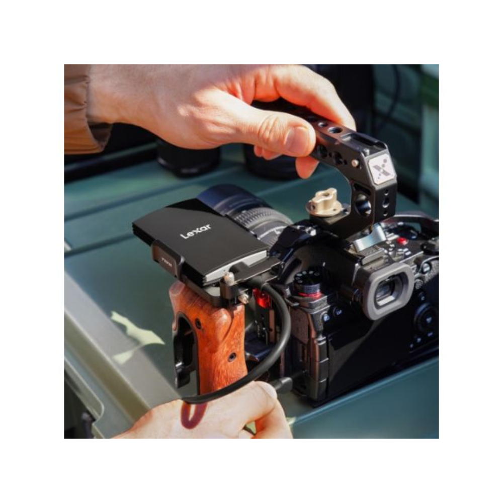 Ręce trzymają aparat z czarnym zewnętrznym dyskiem twardym Lexar. Aparat znajduje się na zielonej powierzchni.