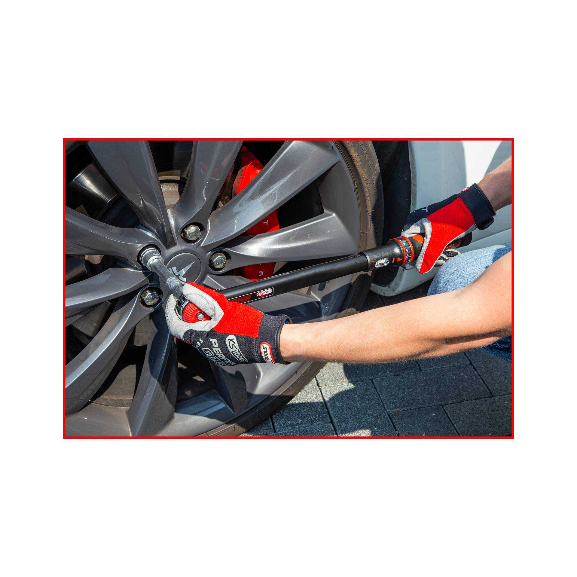 Person benutzt einen Schraubenschlüssel an einem Autorad. Trägt rote Handschuhe. Autorad ist grau mit roten Bremssätteln.