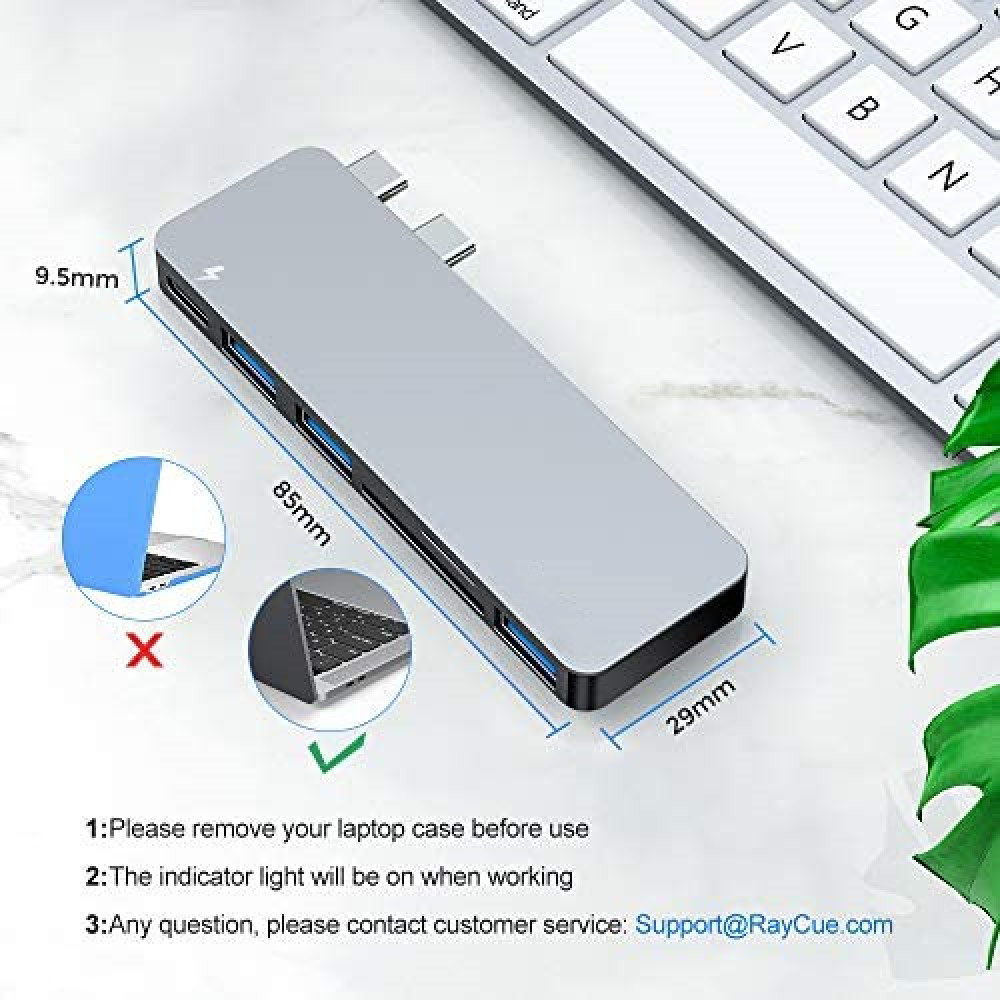 Ein silberner USB-C-Hub wird mit Abmessungen angezeigt. Eine Tastatur und grüne Blätter sind ebenfalls im Hintergrund. Anweisungen stehen unten.