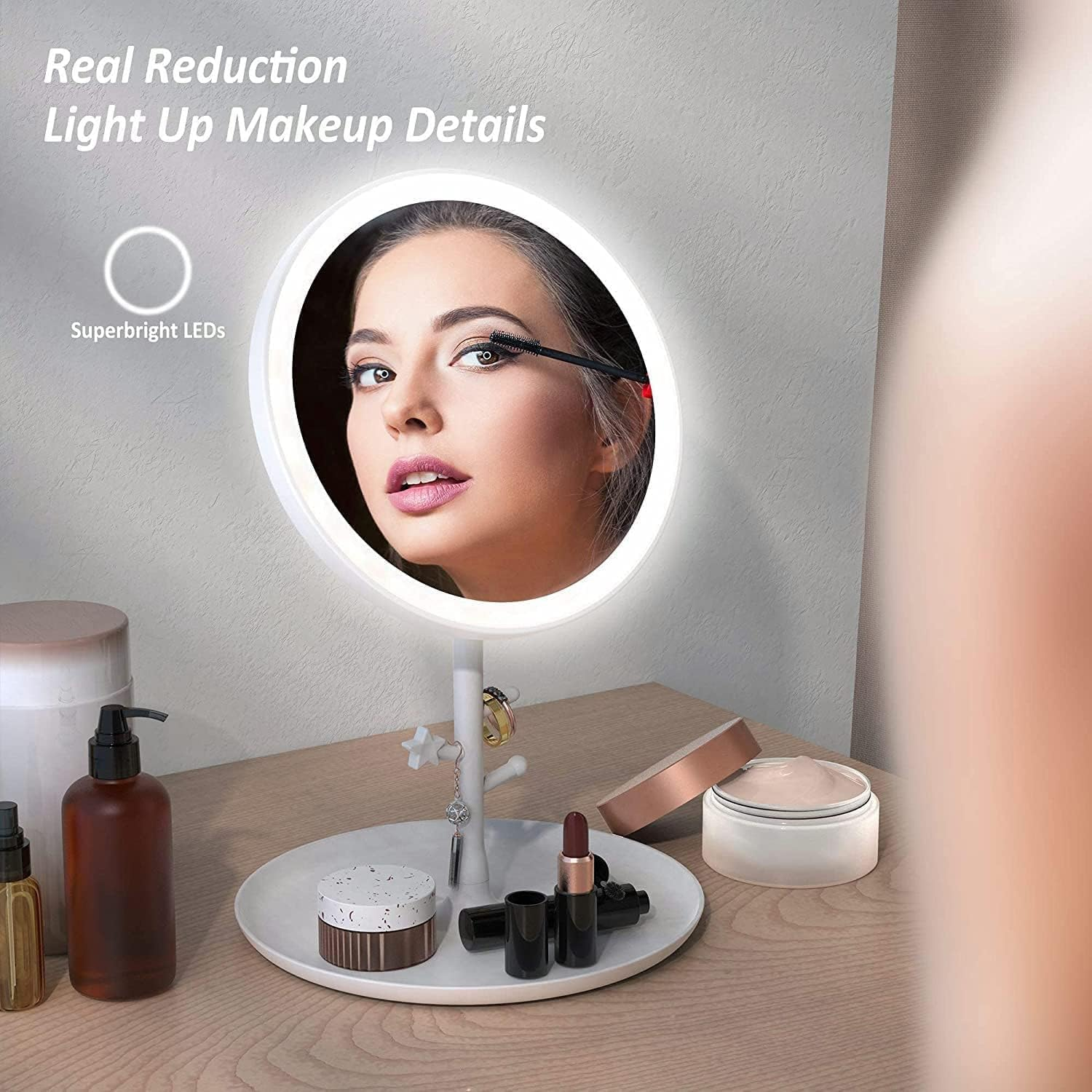 Eine Frau trägt Wimperntusche in einem beleuchteten Schminkspiegel auf. Kosmetika und Accessoires stehen auf einem Tisch. Der Spiegel hat ein weißes Licht.