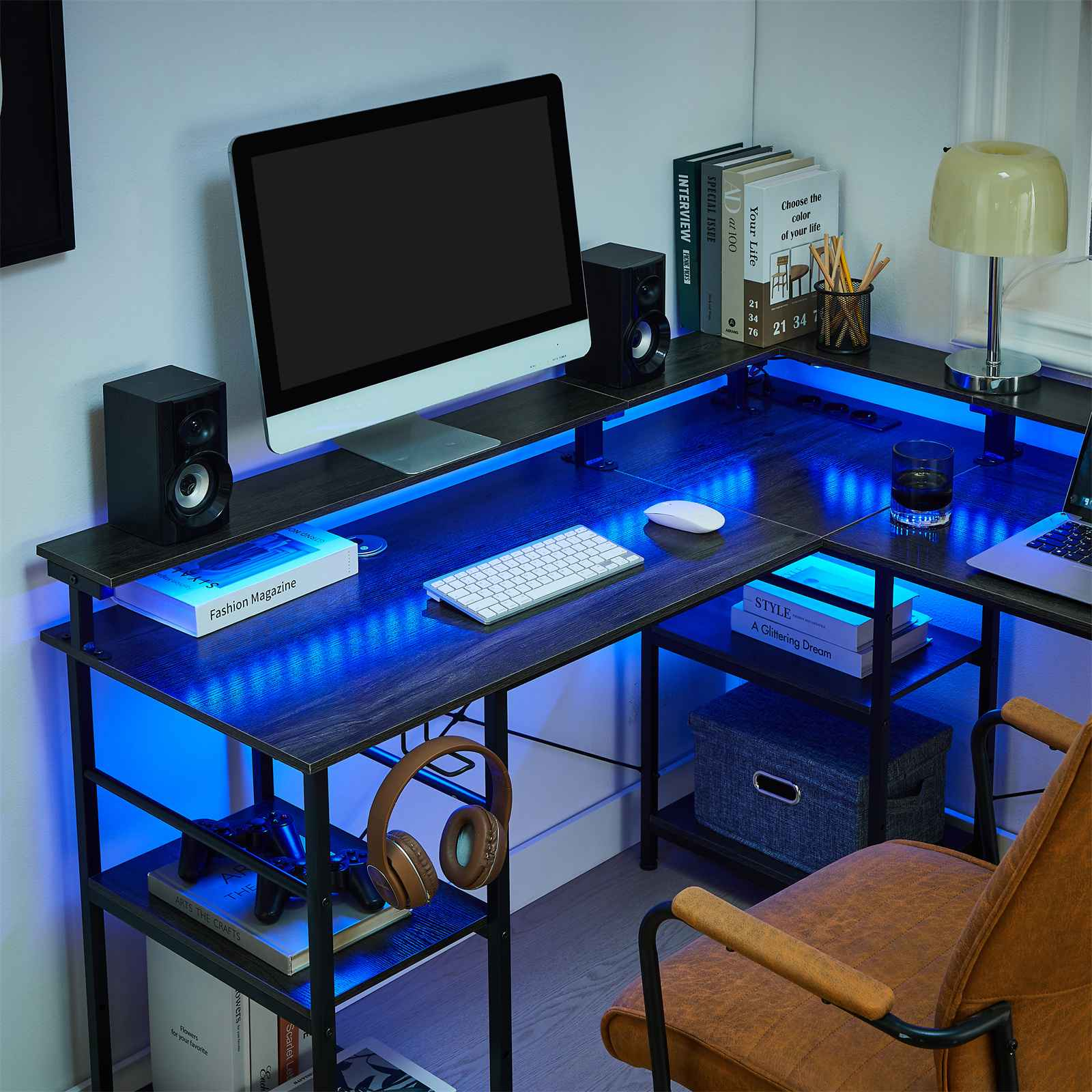 L-förmiger Schreibtisch mit Computer, Lautsprechern, Büchern und Zubehör. Blaue LED-Leuchten beleuchten den Schreibtisch. Brauner Stuhl im Vordergrund.