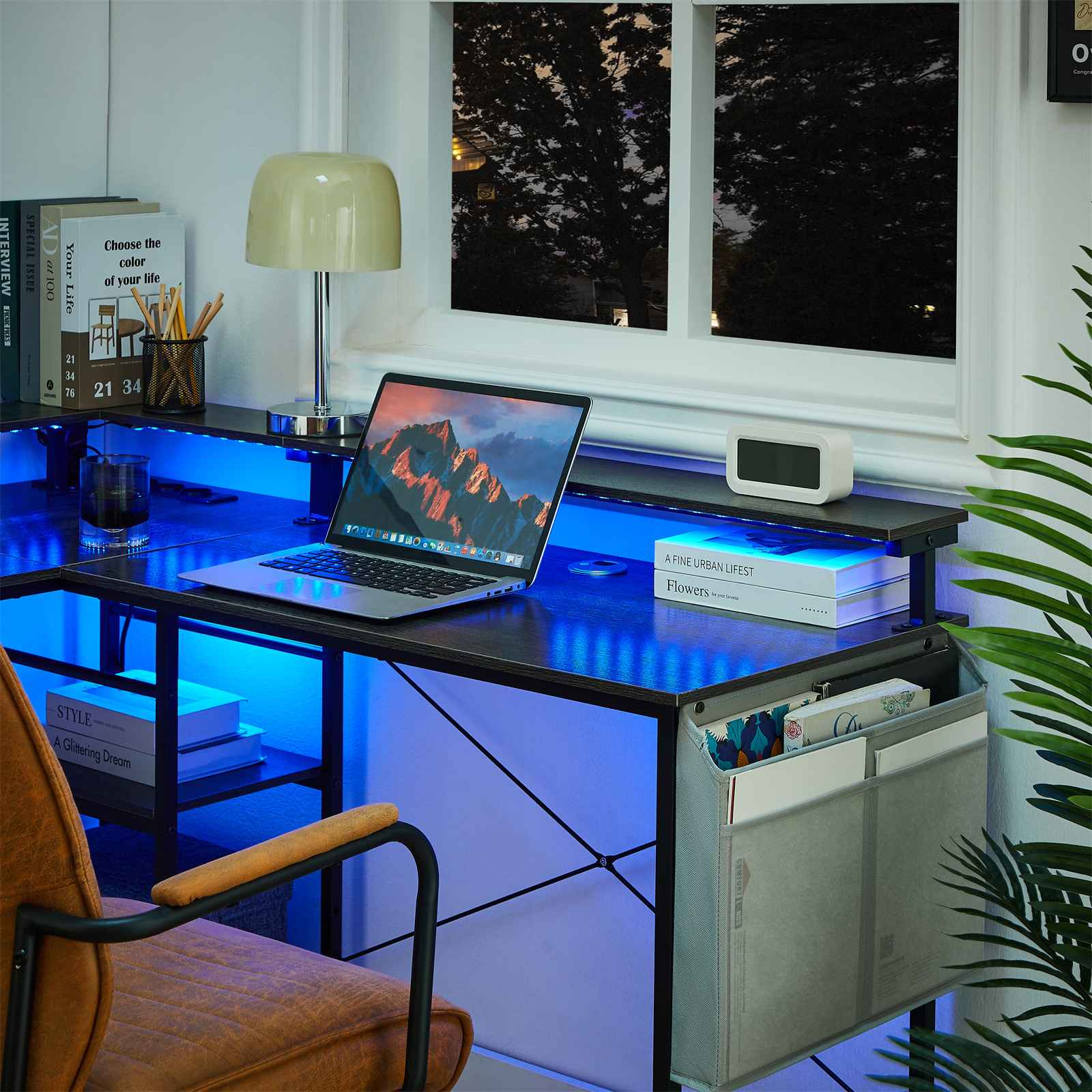 Ein Schreibtisch mit Laptop, Lampe und Büchern. Das Fenster zeigt eine dunkle, baumbestandene Szene. Blaue Beleuchtung beleuchtet den Schreibtisch.