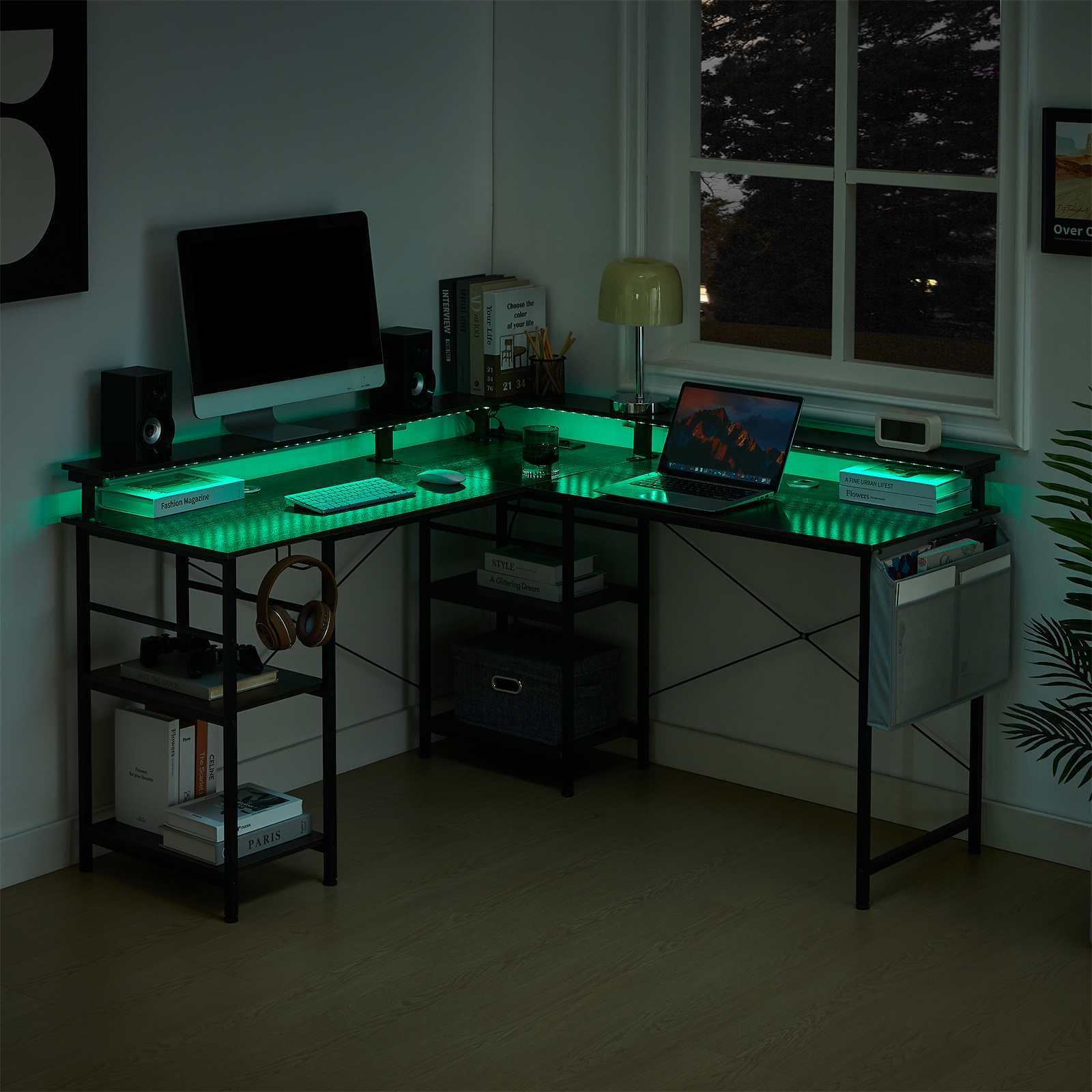 Dunkler Raum mit beleuchtetem Schreibtisch, Computer, Büchern und einem Fenster mit Blick auf Bäume. Grüne Lichter.