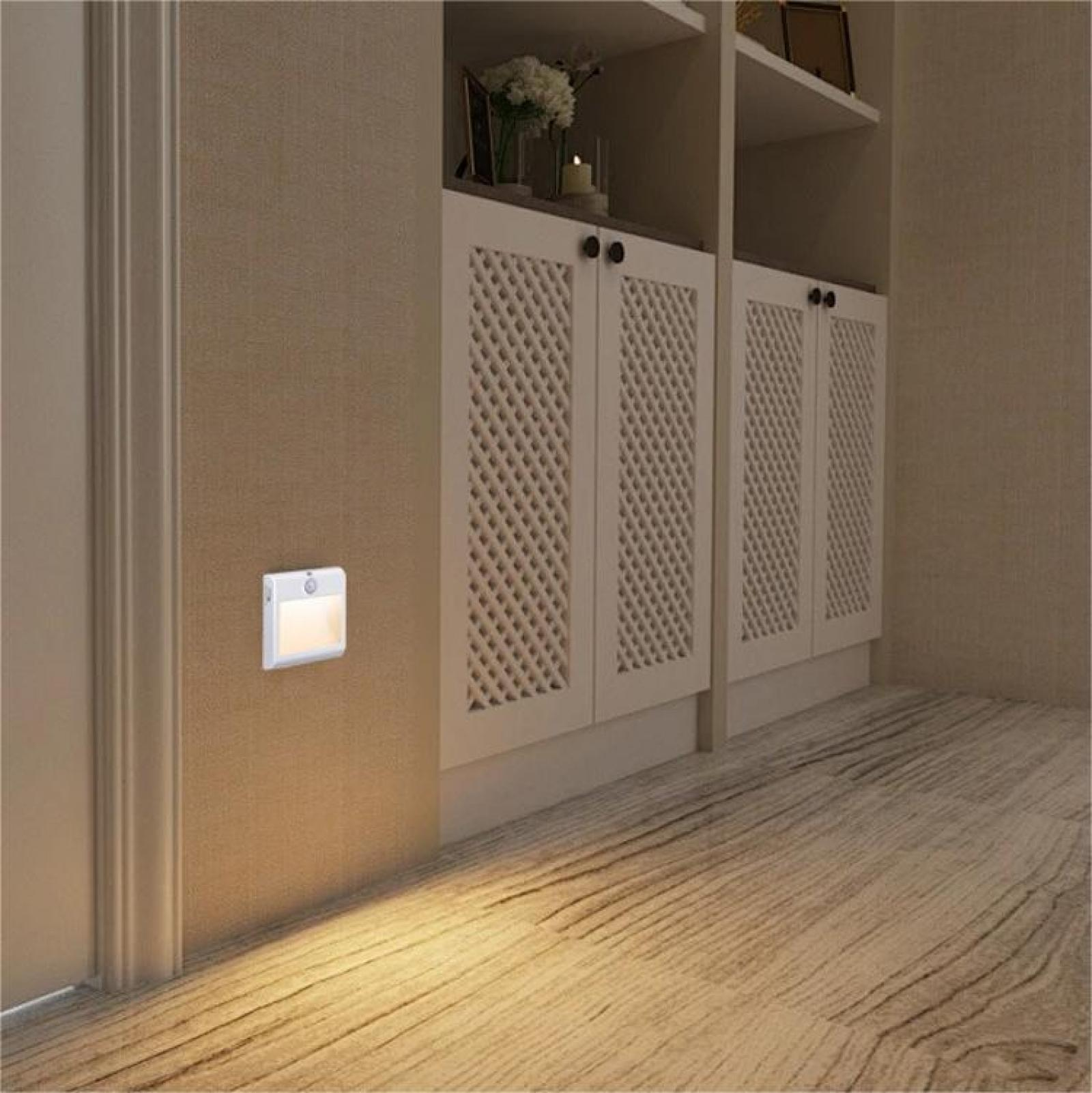 Eine beleuchtete Wandleuchte an einer beigen Wand. Der Holzboden reflektiert das Licht. Hinter der Wand befindet sich ein weißer Schrank mit Gittertüren.