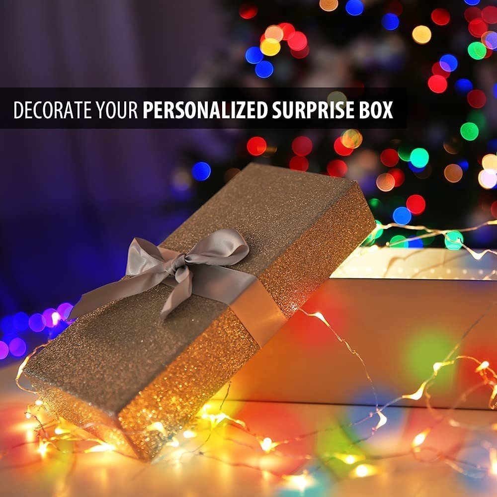 Eine glitzernde goldene Geschenkbox mit silbernem Band ist geöffnet. Bunte Lichter und Bokeh im Hintergrund, mit Text 'DECORATE YOUR PERSONALIZED SURPRISE BOX'.
