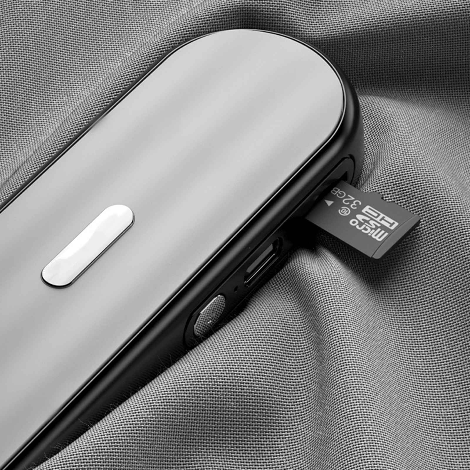 Ein silbernes Gerät mit einer eingelegten 32-GB-Micro-SD-Karte, das auf grauem Stoff liegt. Auf dem Gerät befindet sich ein weißer Knopf.