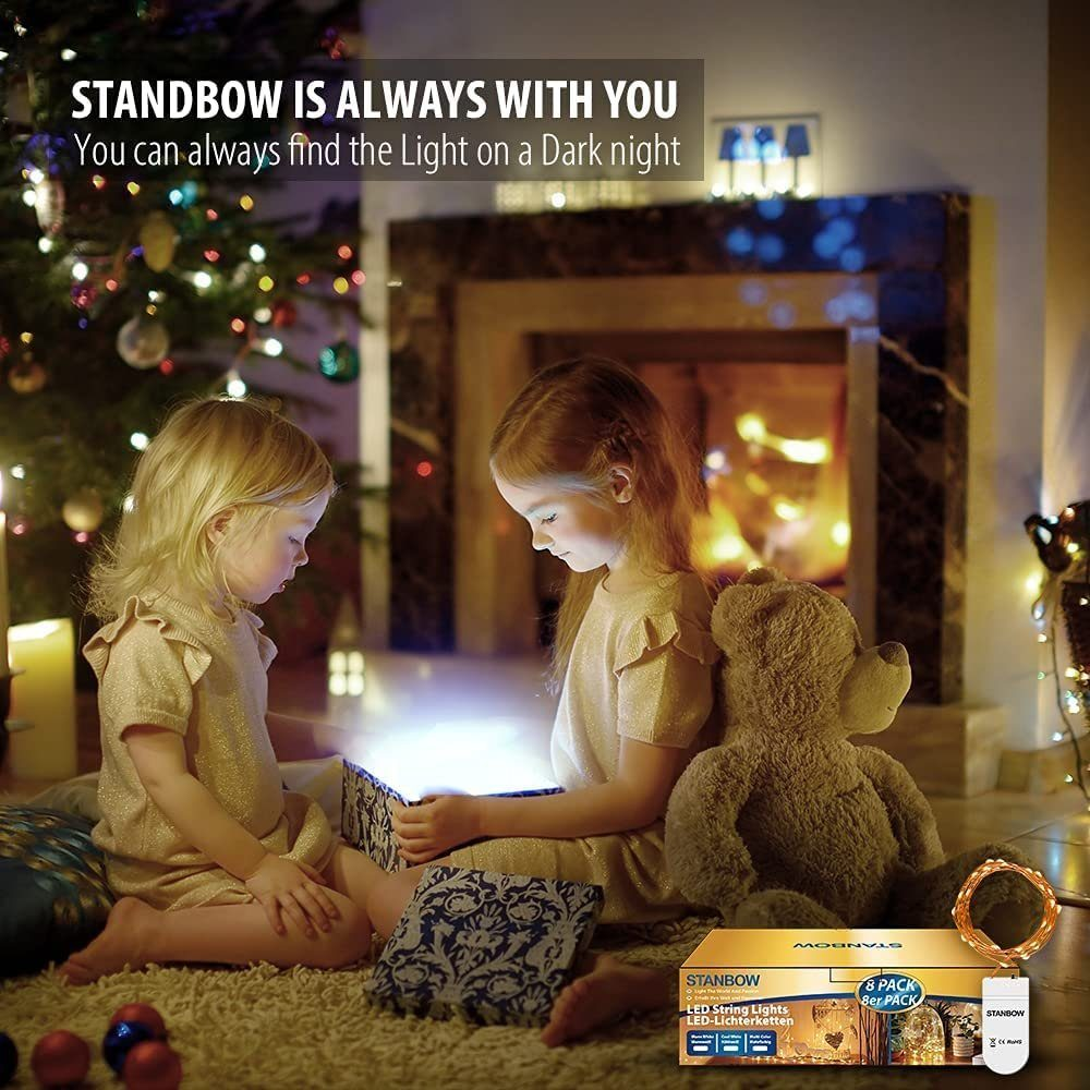 Dwie małe dziewczynki siedzą w pobliżu kominka i choinki, patrząc na świecącą skrzynkę. W pobliżu siedzi pluszowy miś.