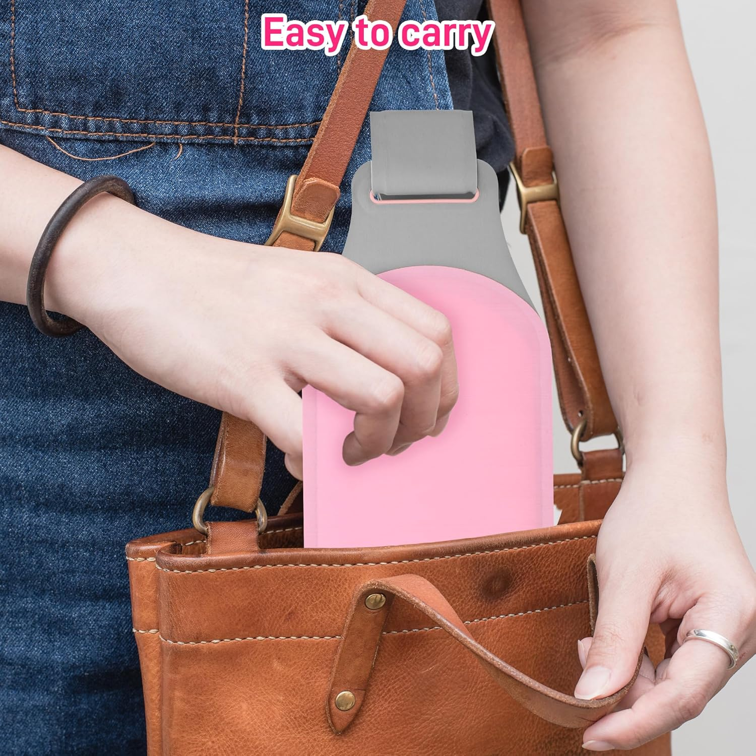 Person hält einen rosa Gegenstand in einer braunen Ledertasche mit grauem Riemen und Jeans-Hintergrund.