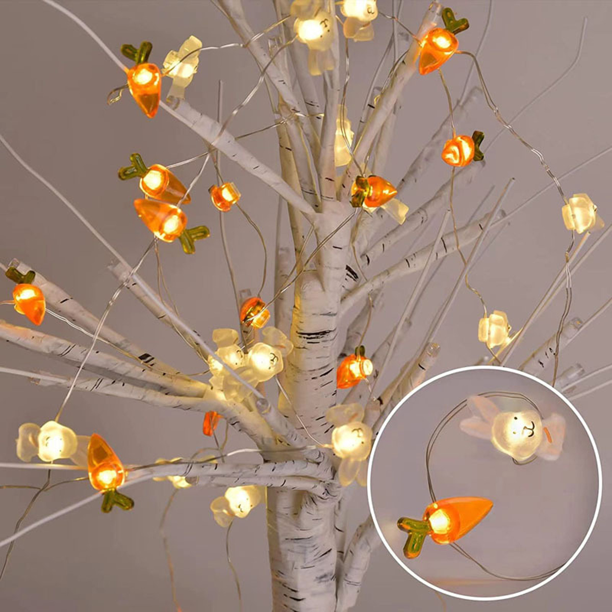 Lichterkette an einem weißen Baum. Die Lichter haben die Form von Karotten und Kaninchen, orange und weiß. Der Hintergrund ist hellgrau.
