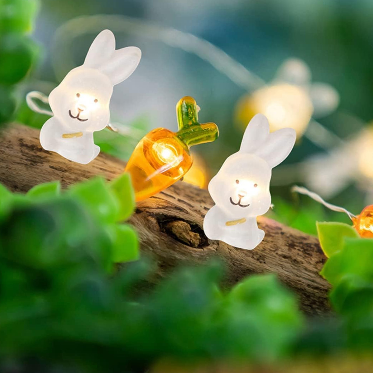 Lichterketten mit Hasen- und Karottenformen. Sie liegen auf einem Ast mit grünen Blättern. Einige Lichter sind unscharf.