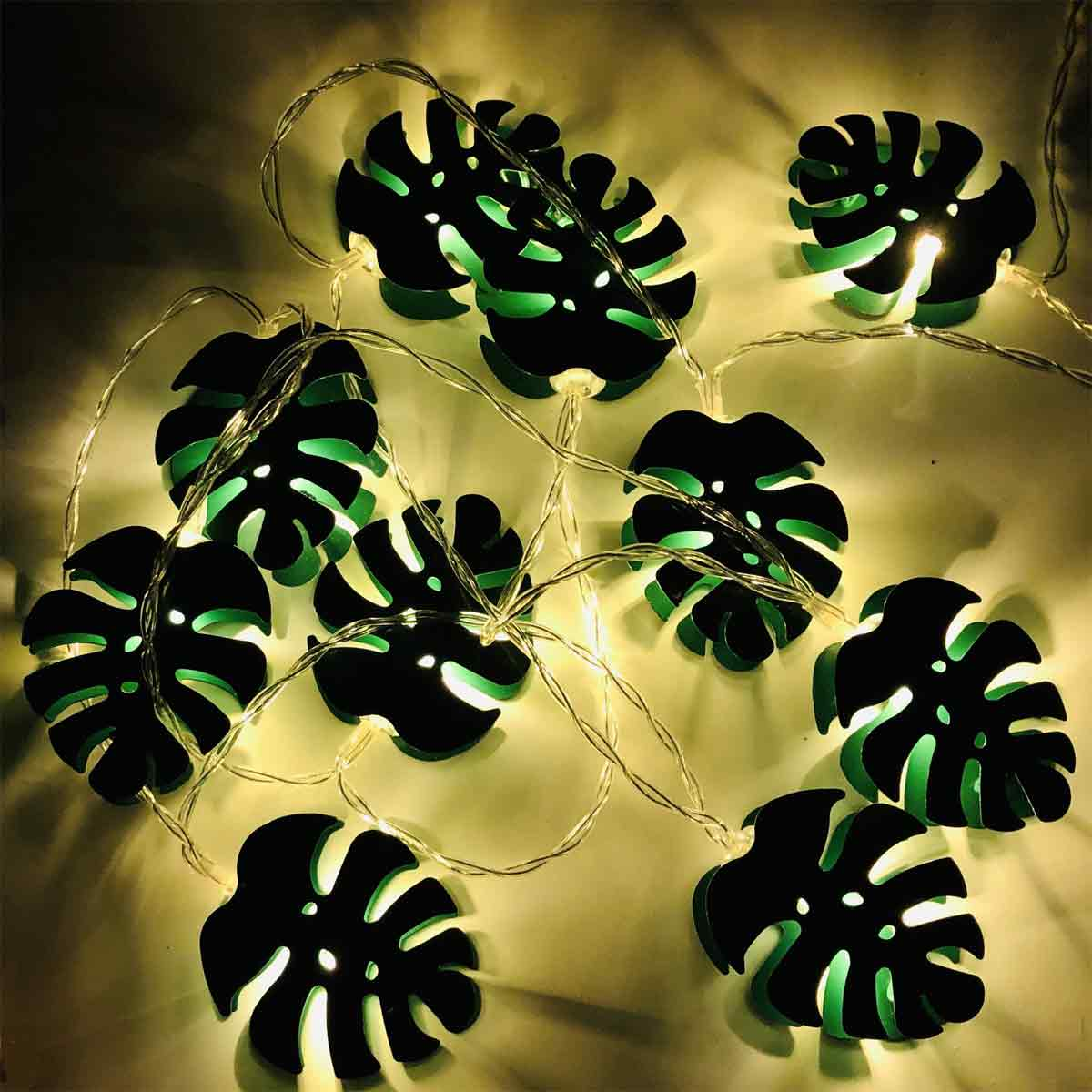 Eine Lichterkette in Blattform. Schwarze Blätter mit grünen Zentren sind beleuchtet. Der Hintergrund ist eine weiche, gelb getönte Oberfläche.