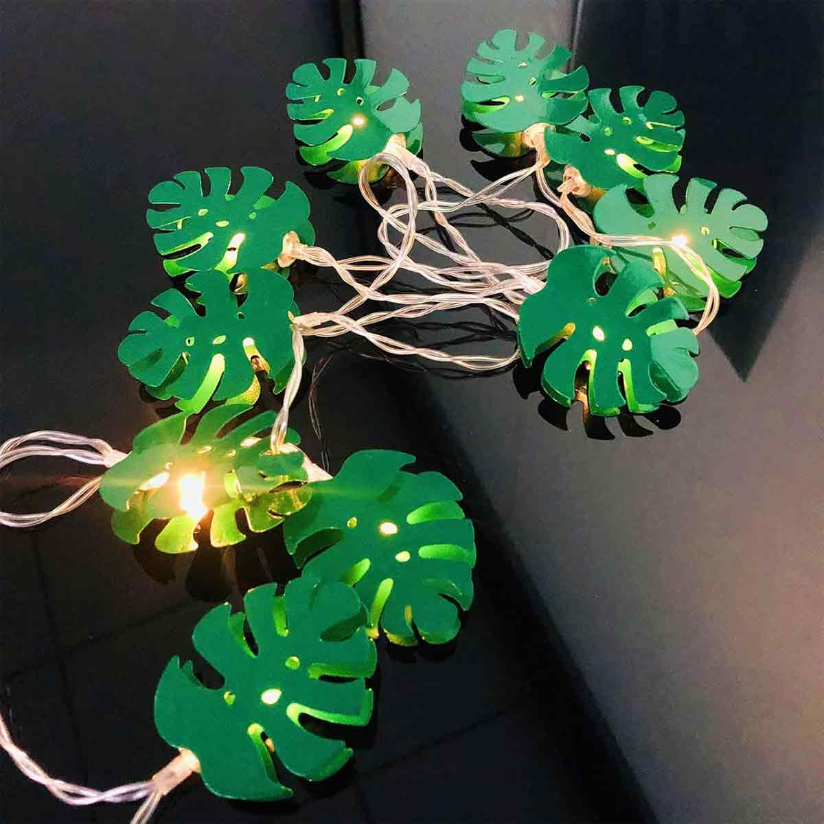 Grüne Monstera-Blatt-Lichterkette. Blätter leuchten. Klarer Draht. Schwarzer Hintergrund.