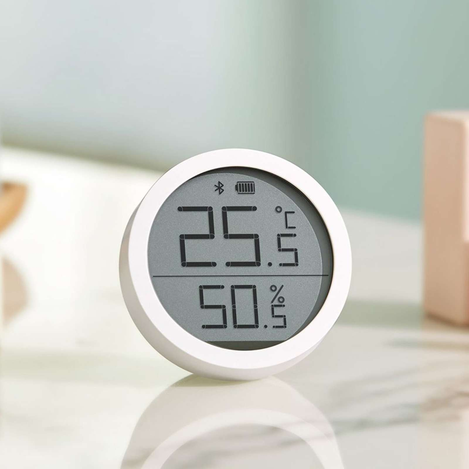 Weißes, rundes digitales Thermometer zeigt 25,5 Grad Celsius und 50,5 % Luftfeuchtigkeit an. Grauer Bildschirm, weißer Rahmen, heller Hintergrund.