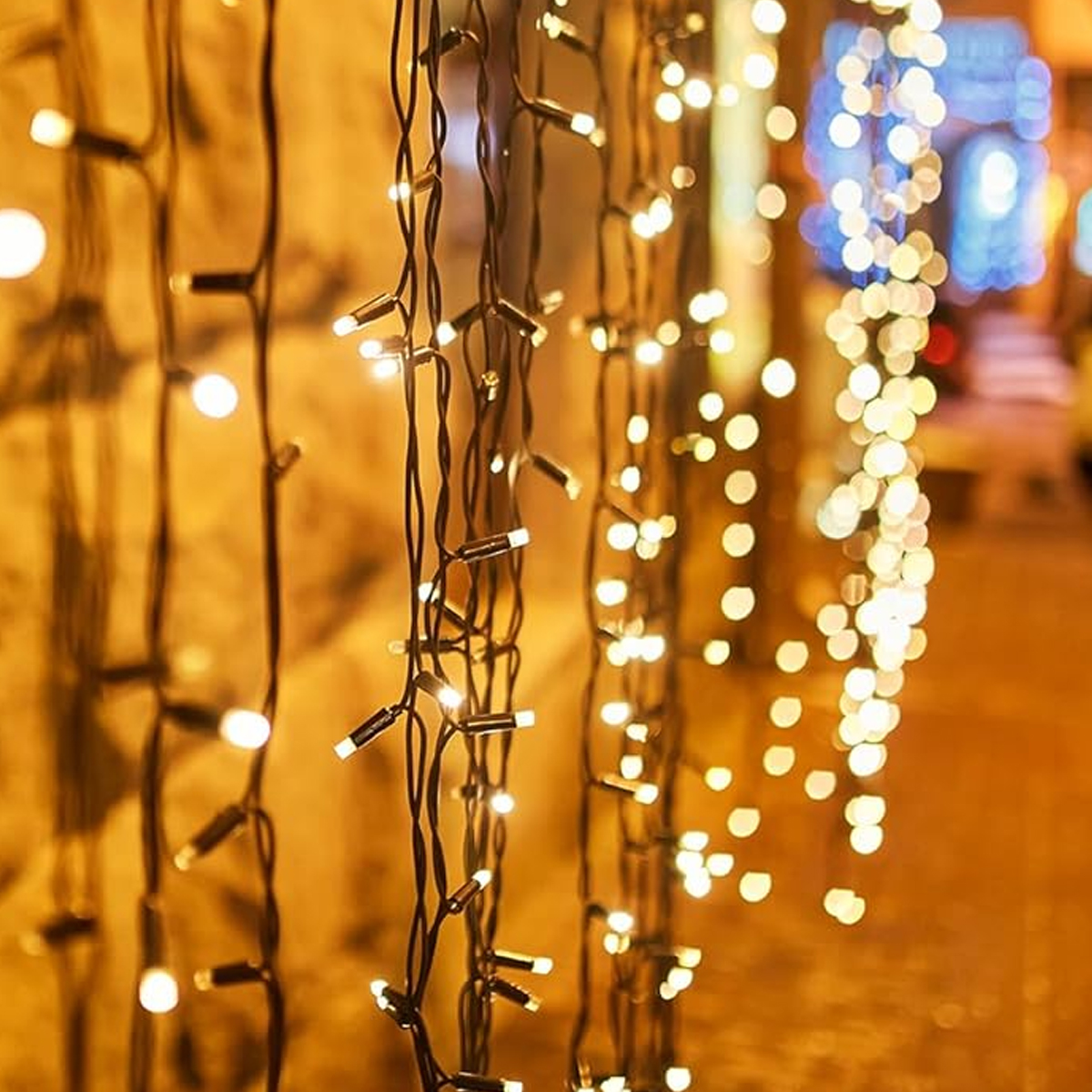 Hängende Lichterketten. Warmweiße Lichter an schwarzen Drähten. Verschwommener Hintergrund mit Lichtern und Gebäuden.